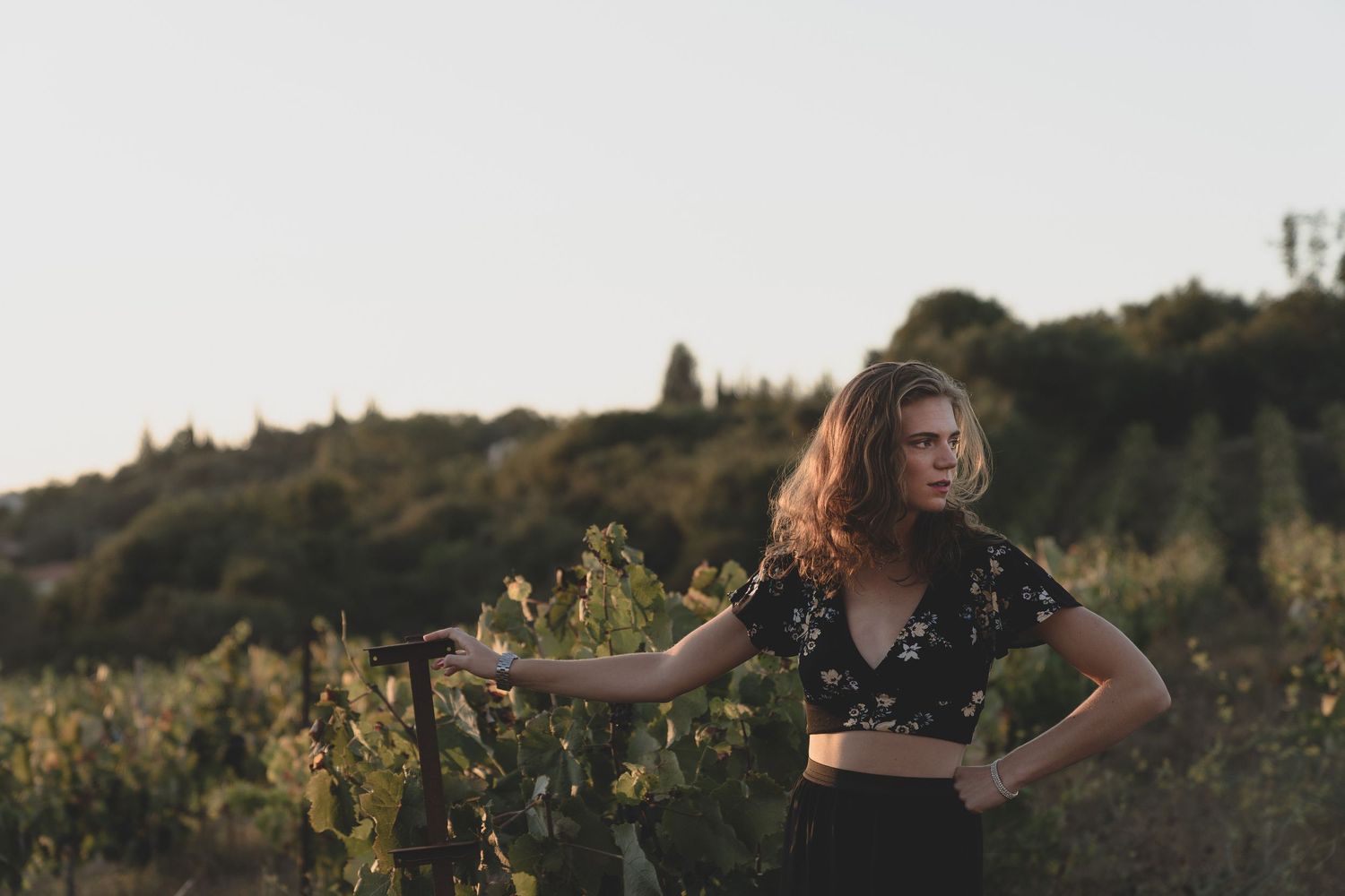 Person in a black crop top poses confidently in a vineyard at sunset.