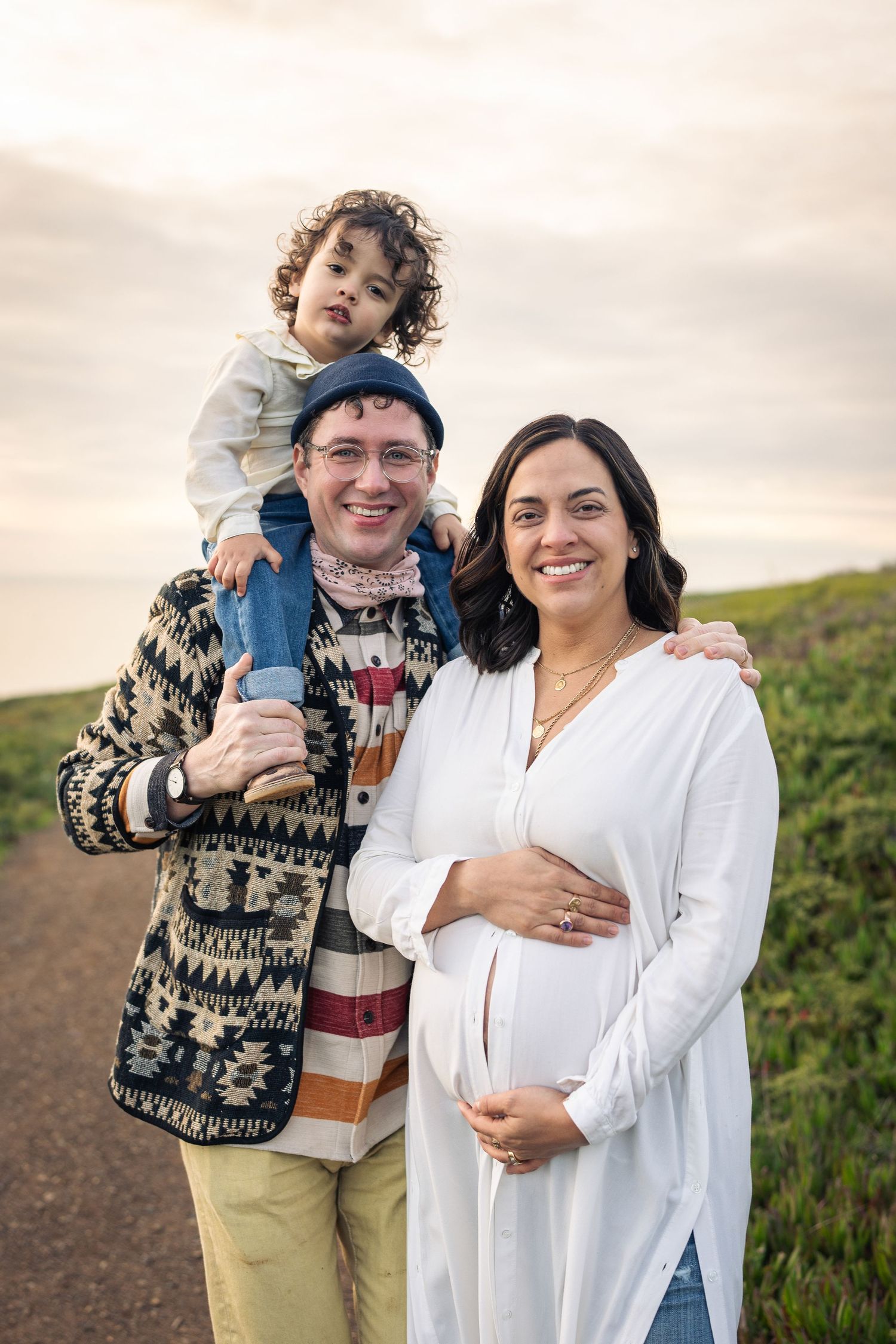 Outdoor portrait of a happy family on coastal trail with expecting mother in white dress.