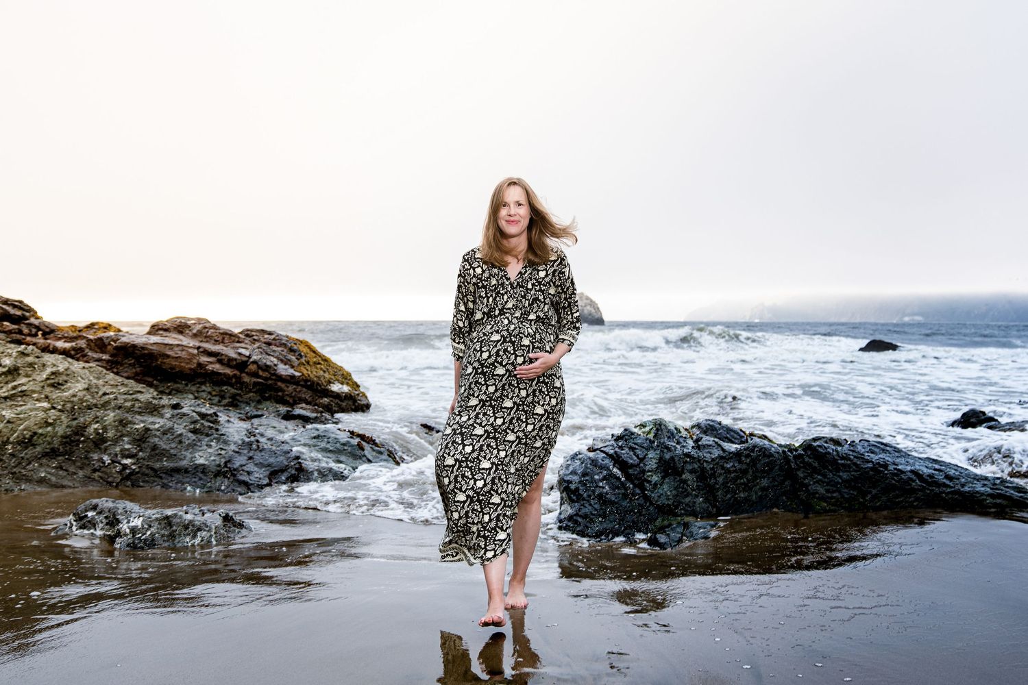 A flowy floral dress catches the ocean breeze as waves crash against rocky coastal cliffs.