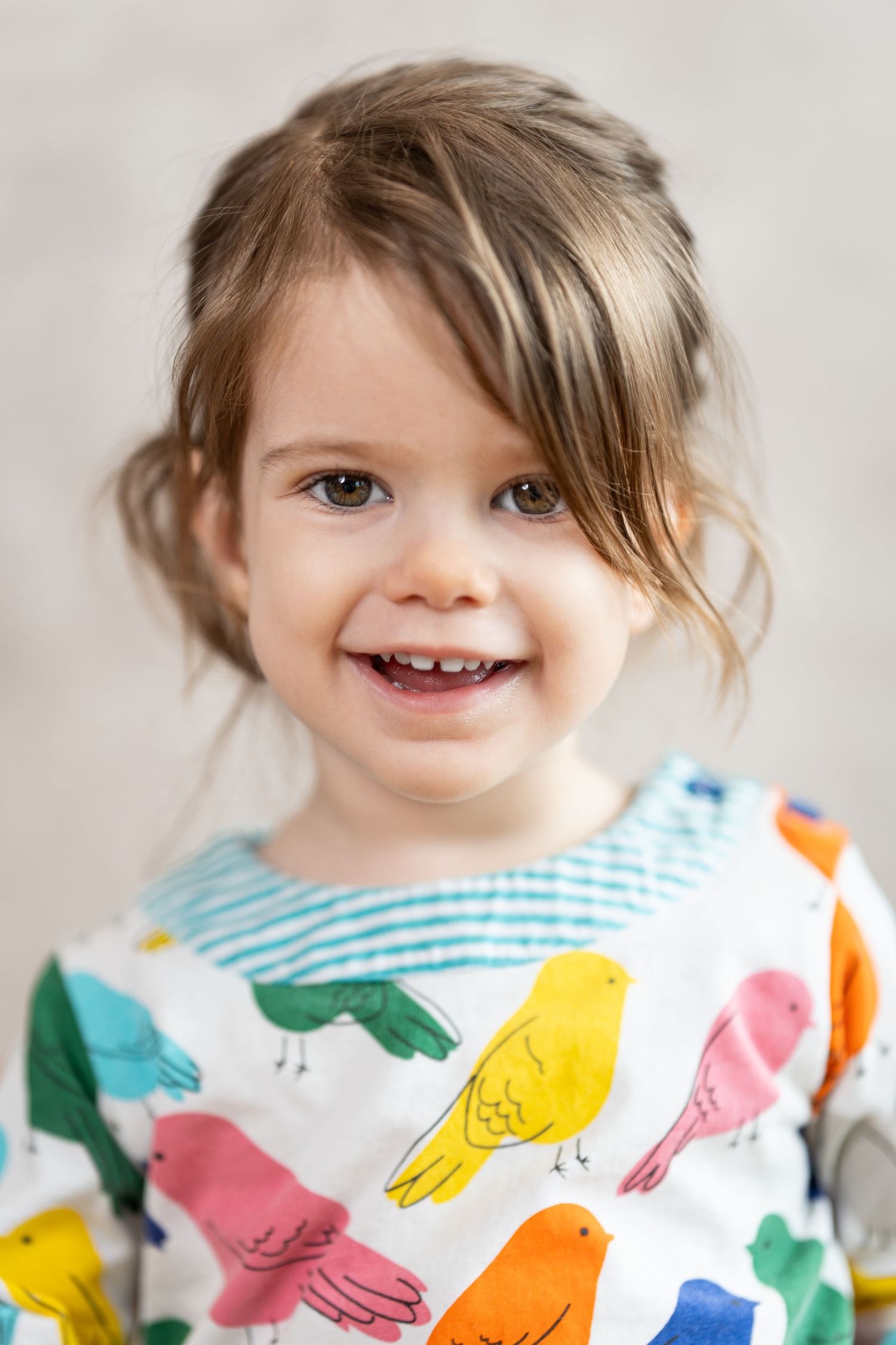 Child wearing a colorful bird-patterned shirt smiles brightly against a light background.