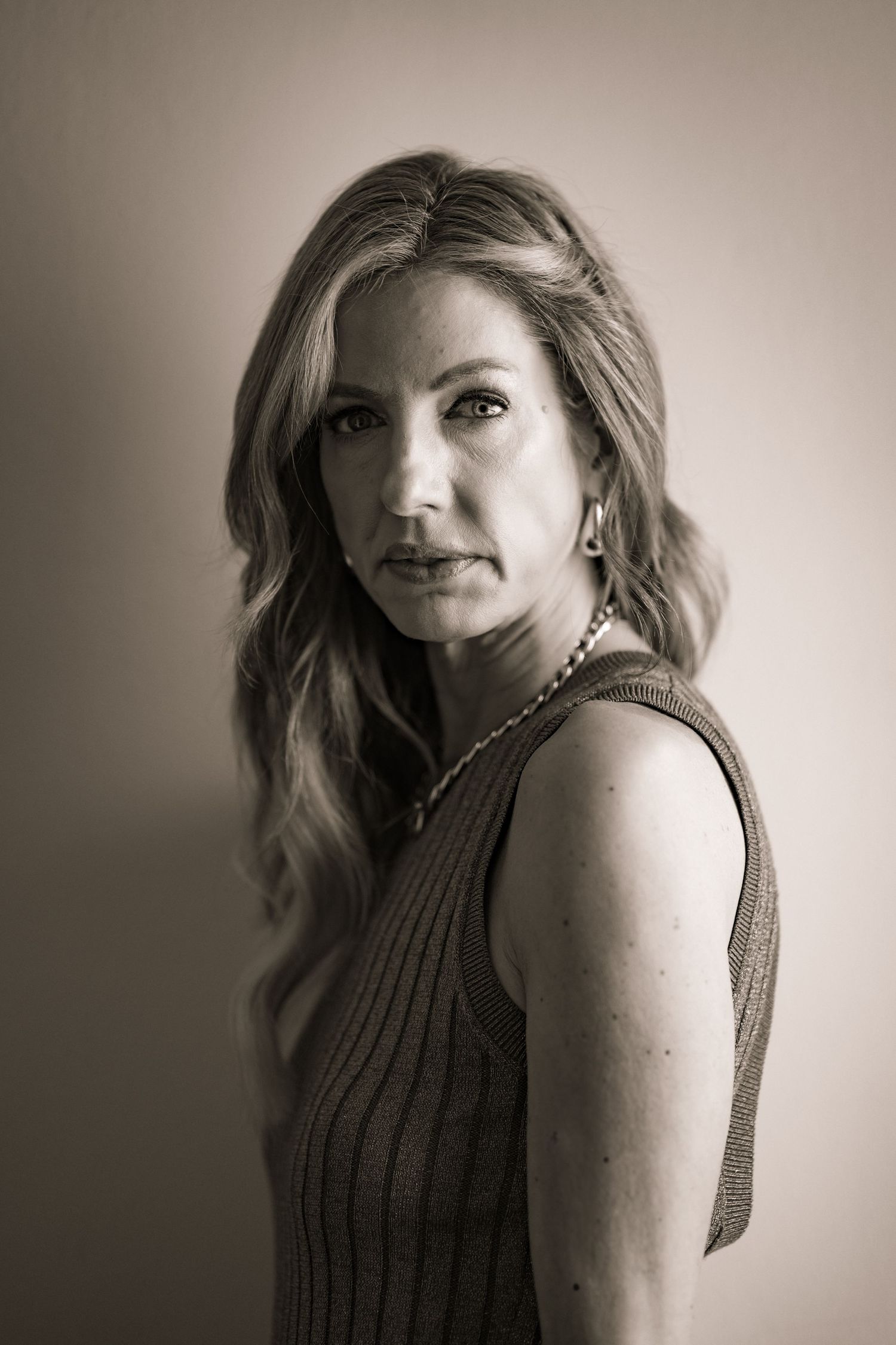 A portrait of someone in a brown sleeveless sweater against a neutral background.