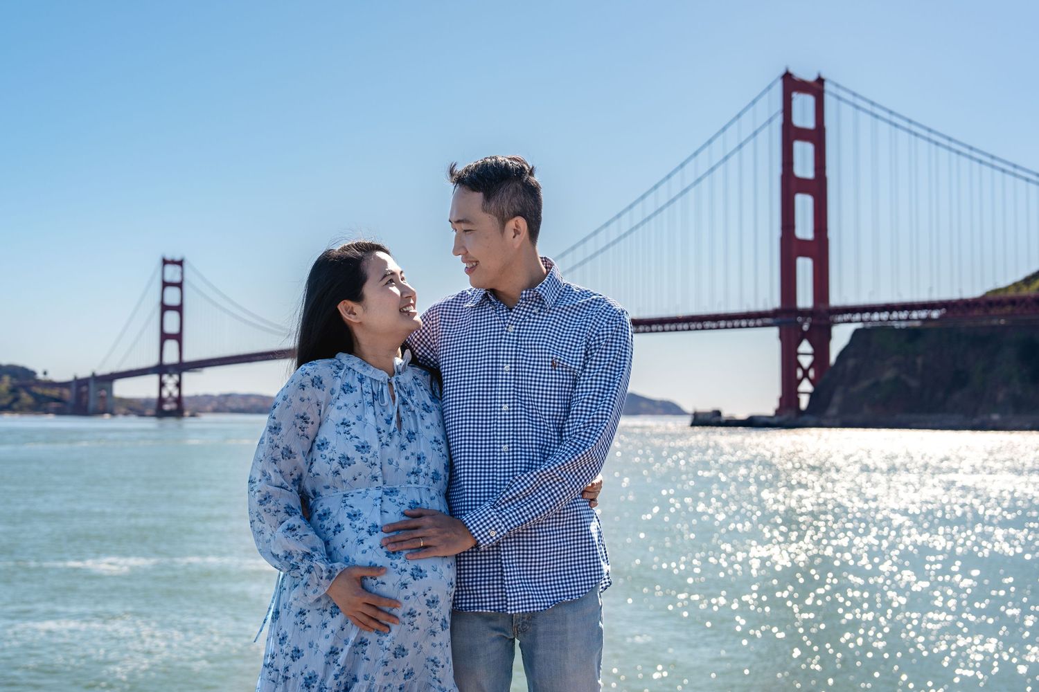 Expectant couple shares a joyful moment by the Golden Gate Bridge in San Francisco.