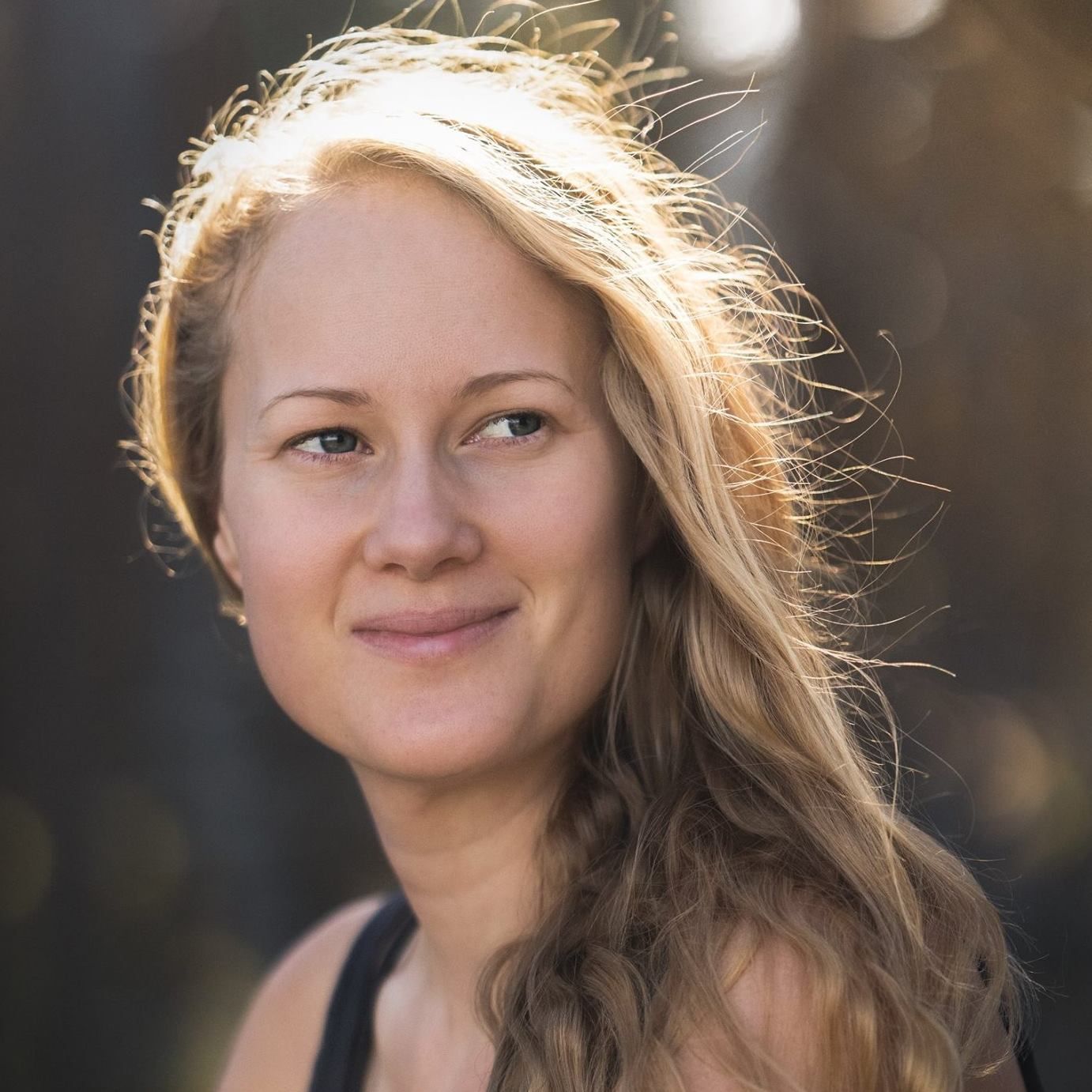 A natural outdoor portrait of someone with windswept hair in golden sunlight.