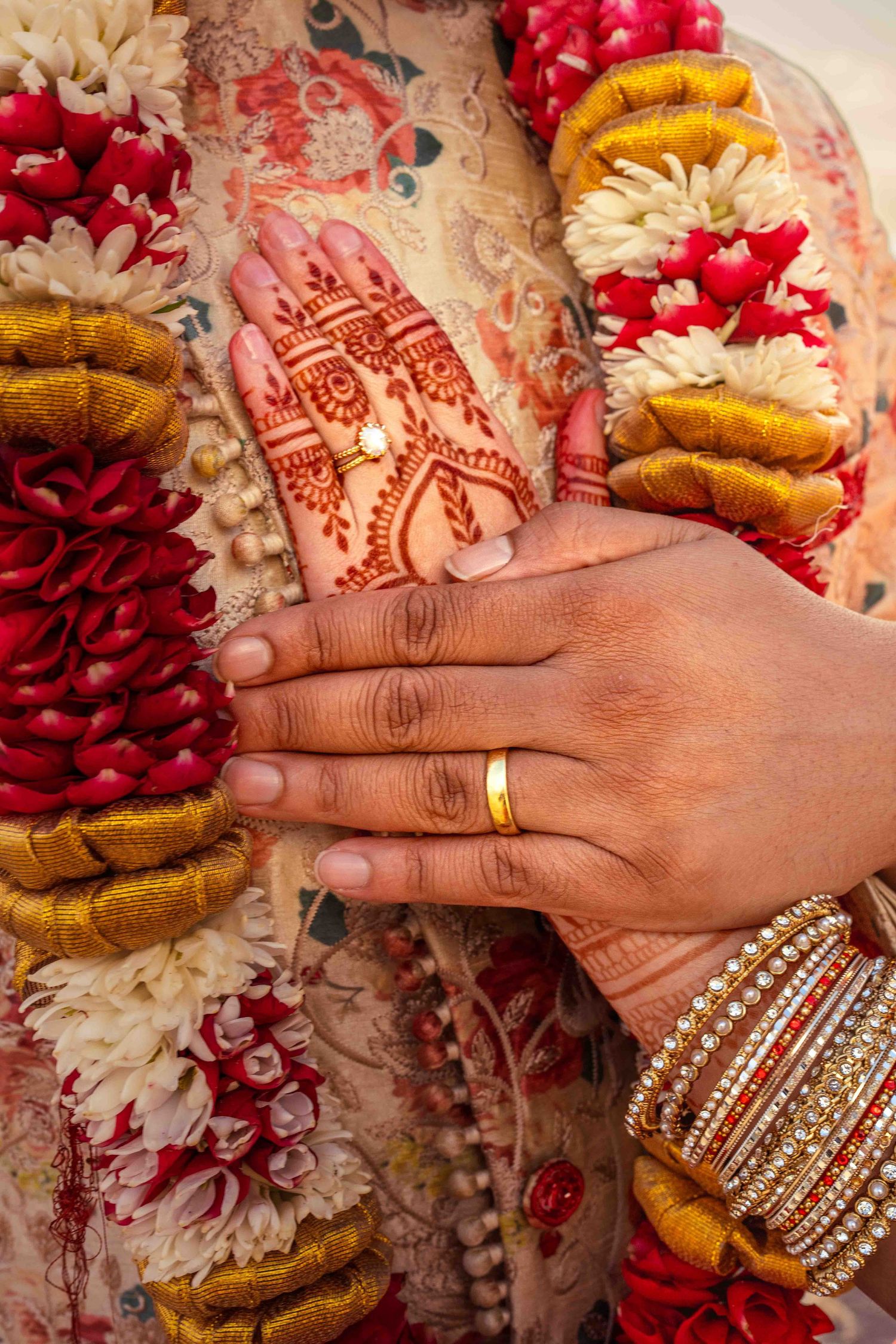 Intricate henna design on a hand adorned with bangles and floral garlands in red and gold.