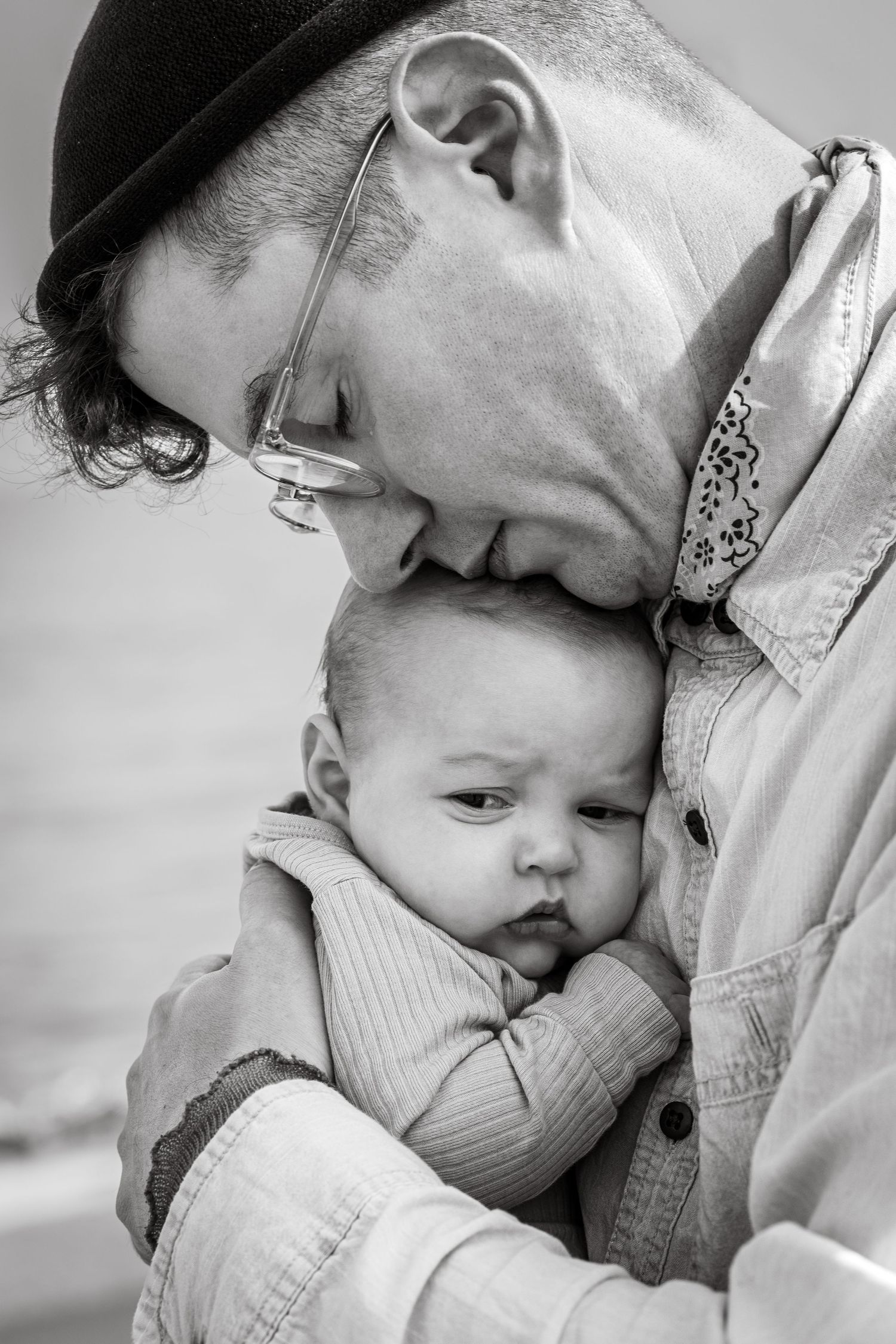 A tender black and white portrait showing affectionate moments between parent and infant in close embrace.