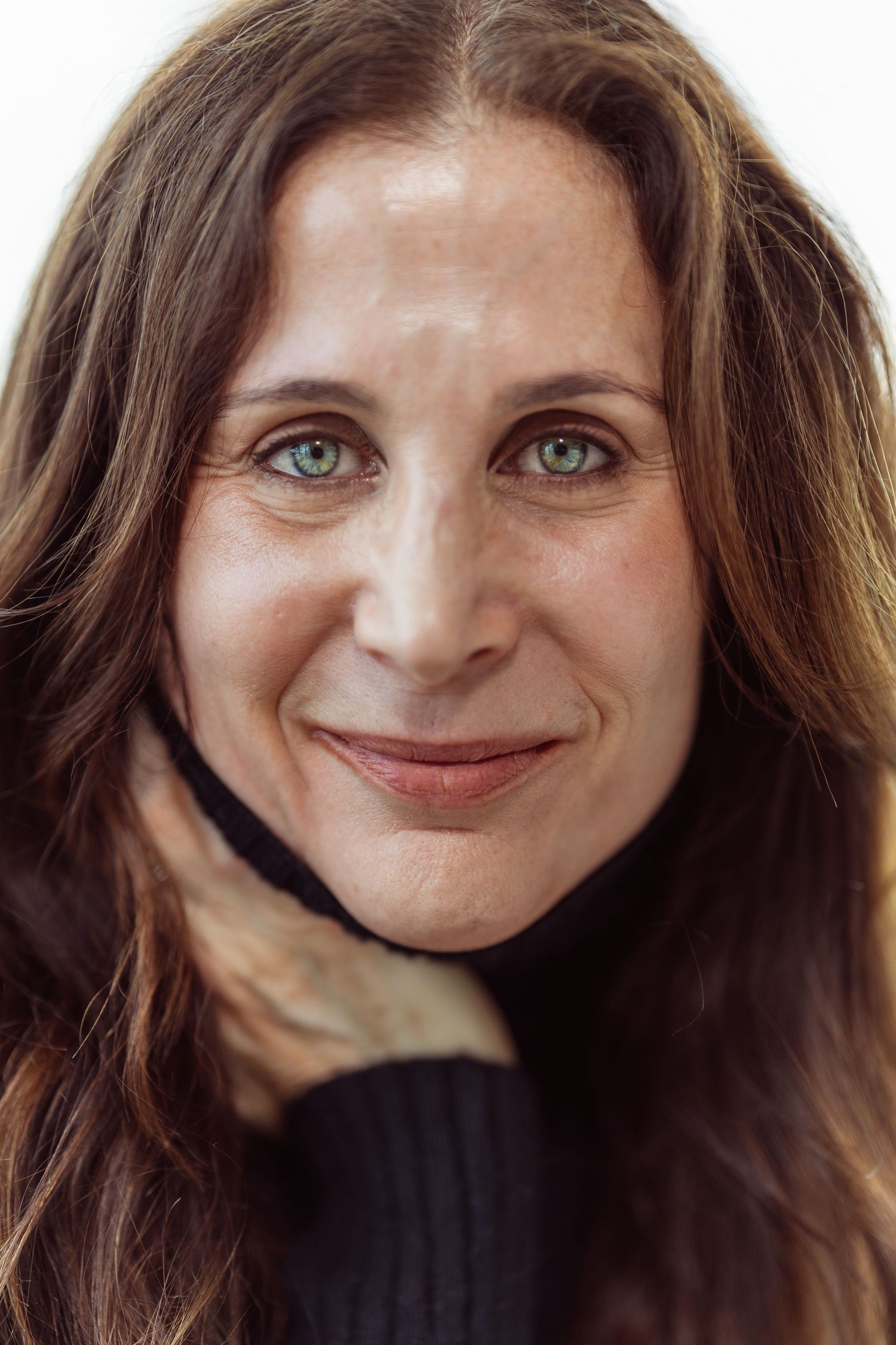 A close-up portrait showing bright green eyes and long dark hair against a light background.