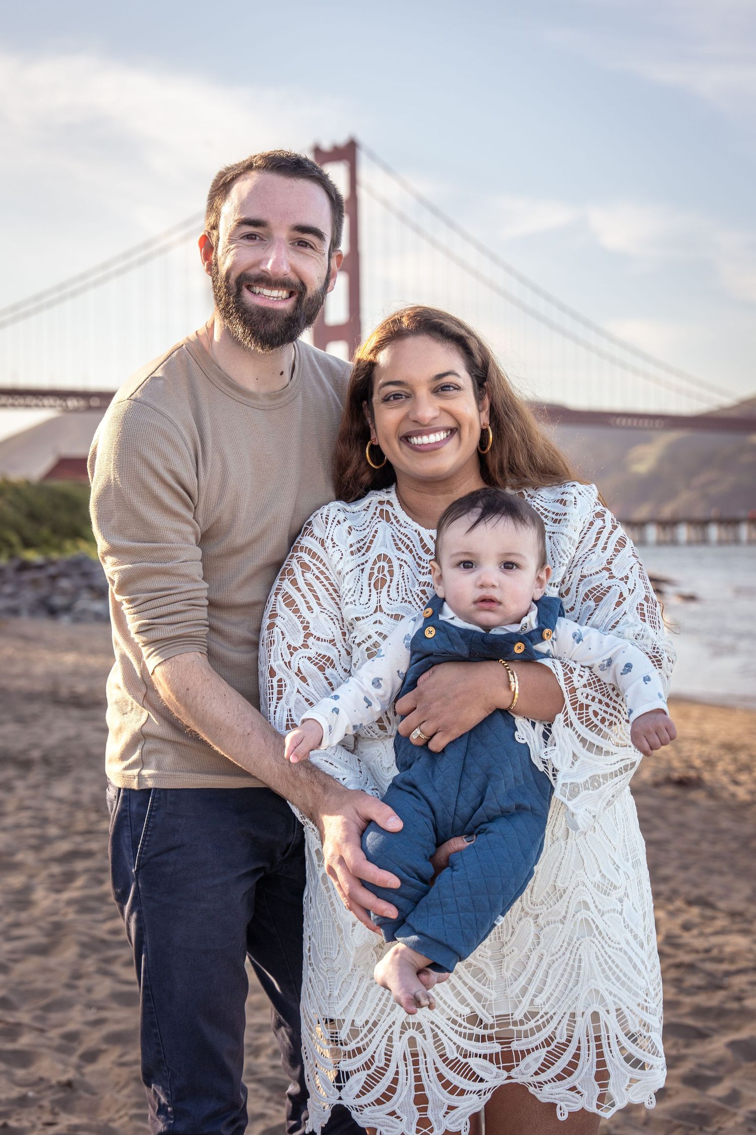 A family shares joyful moments together on a beach with the Golden Gate Bridge visible in the background.