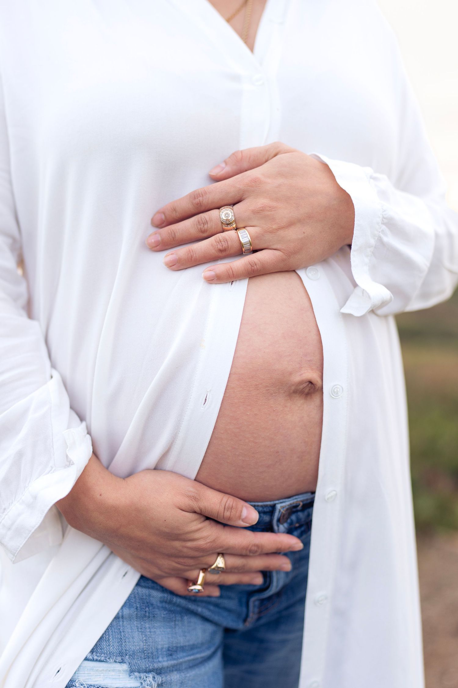 Close up of hands showing engagement ring and pregnant belly in white shirt.
