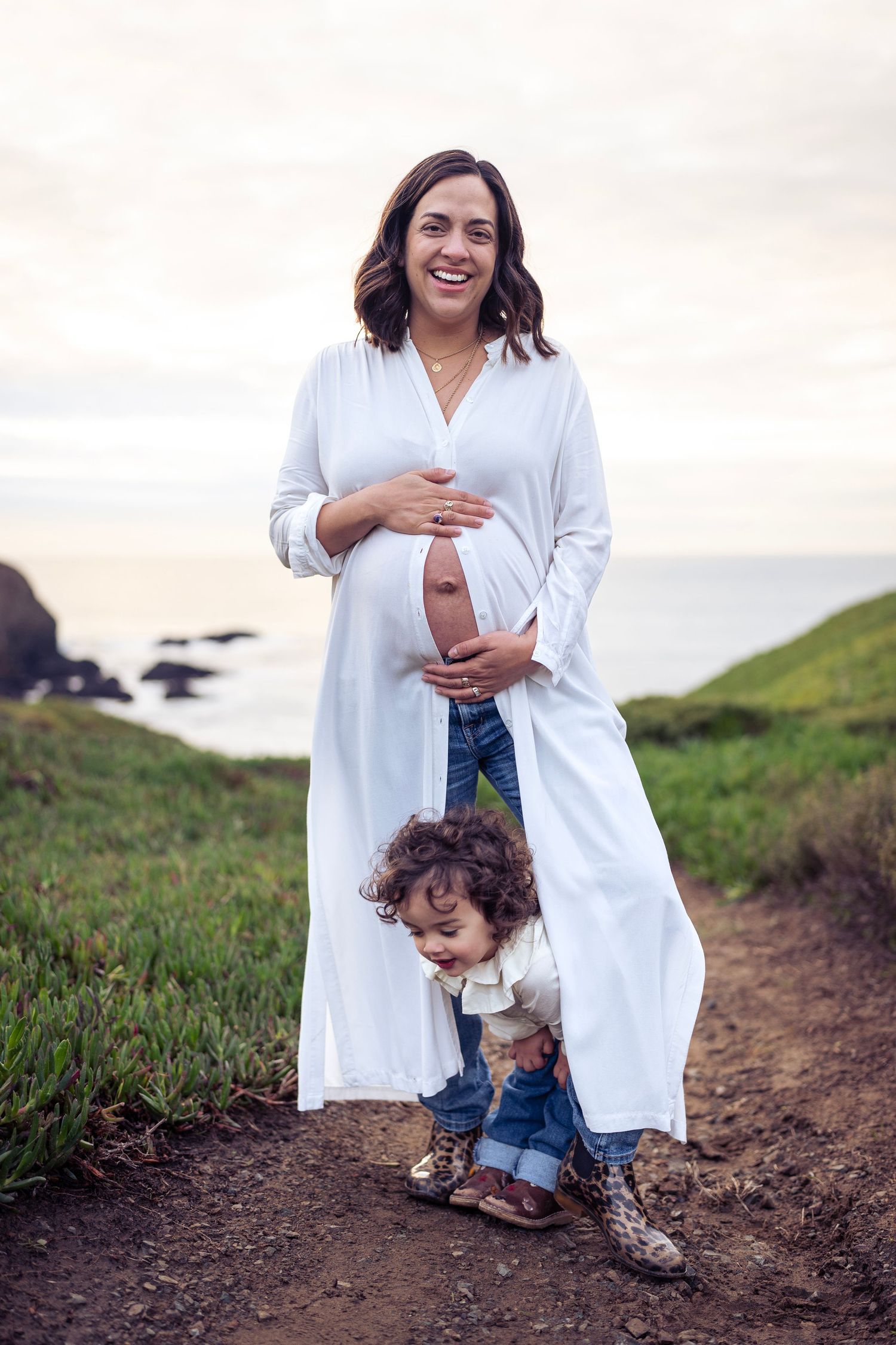Mother and toddler walking along coastal trail during pregnancy photoshoot.