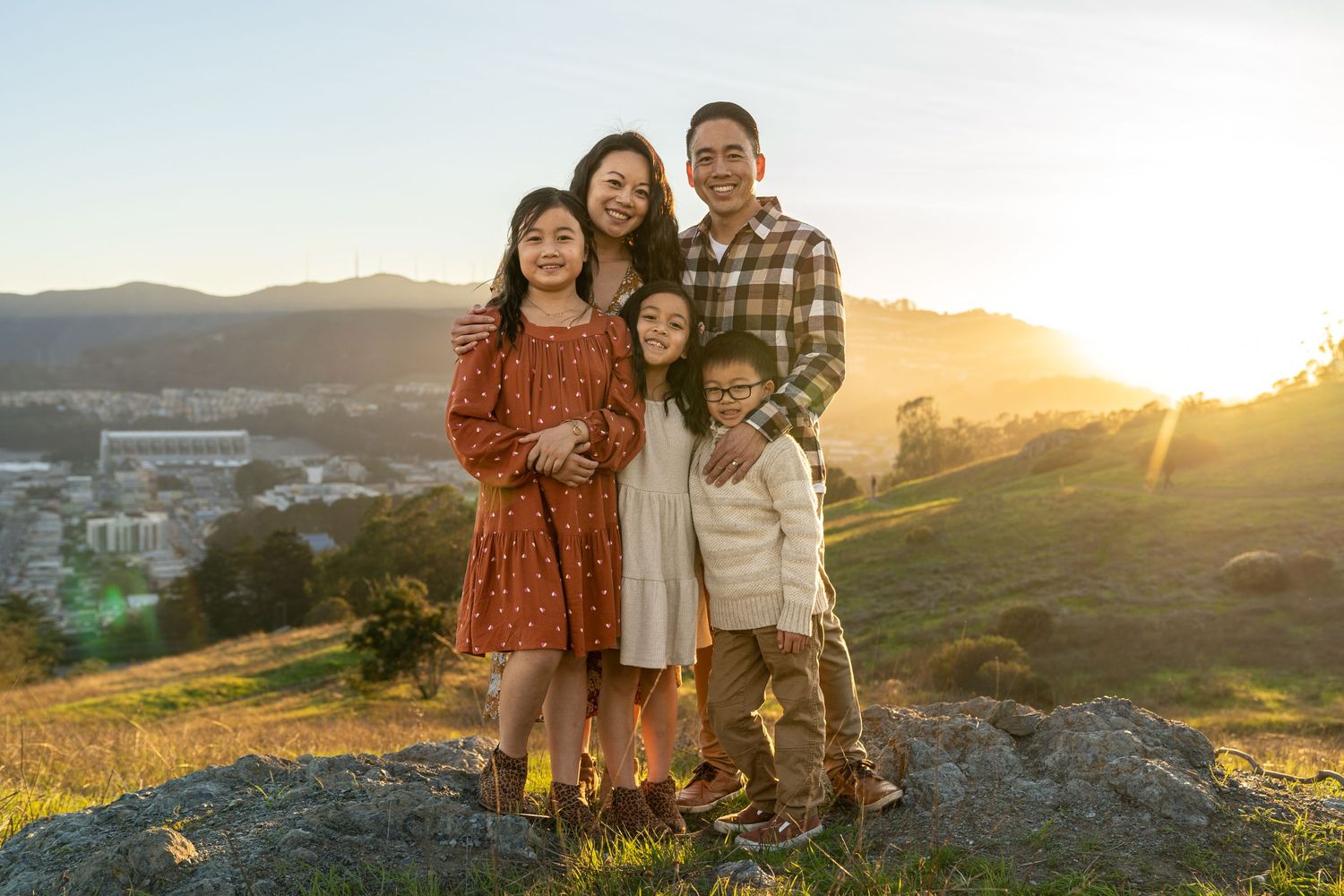 Family portrait on rocky overlook with golden sunset lighting behind them.