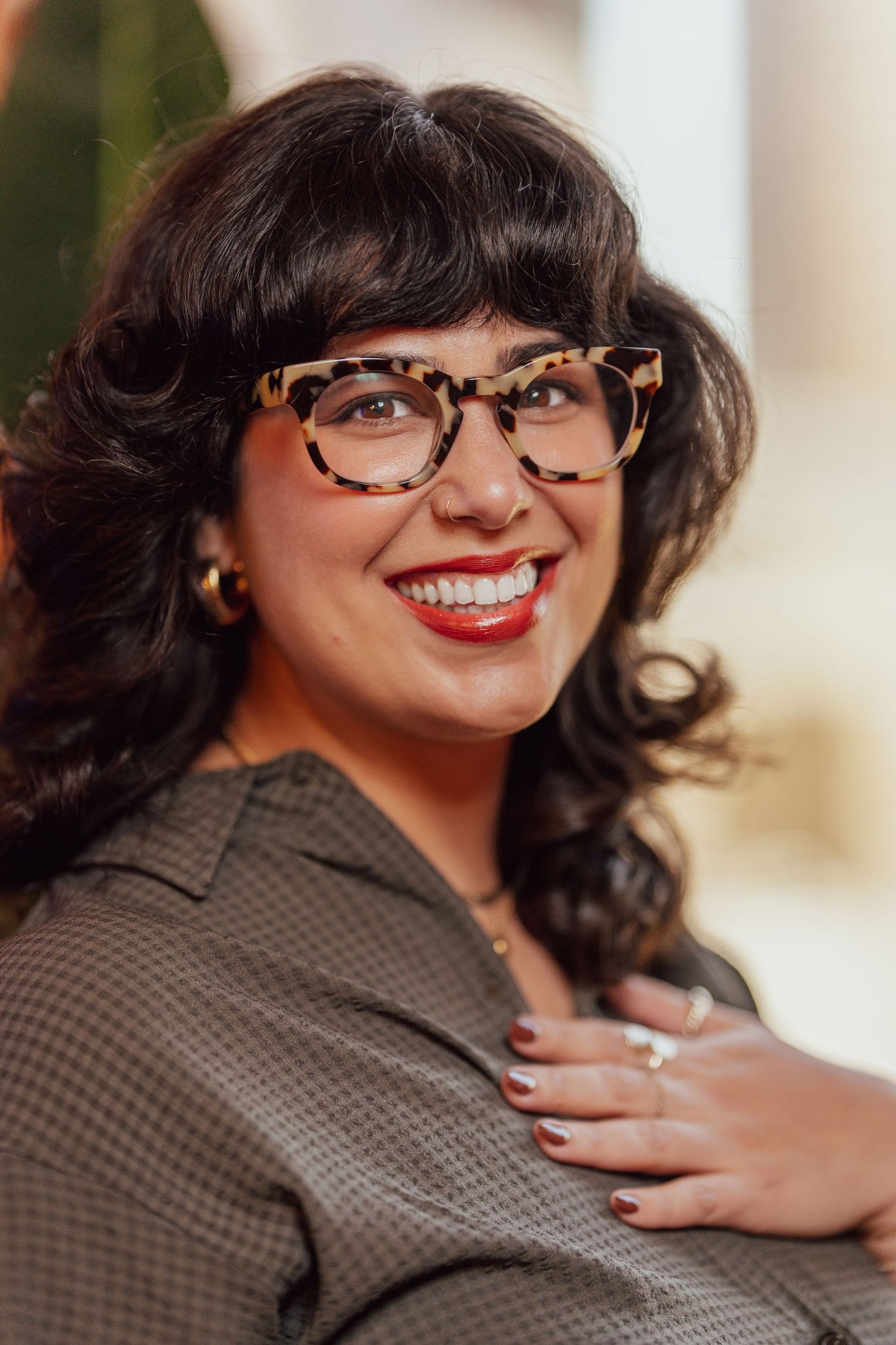A joyful portrait featuring tortoise shell glasses, dark curls, and a bright red lipstick smile.
