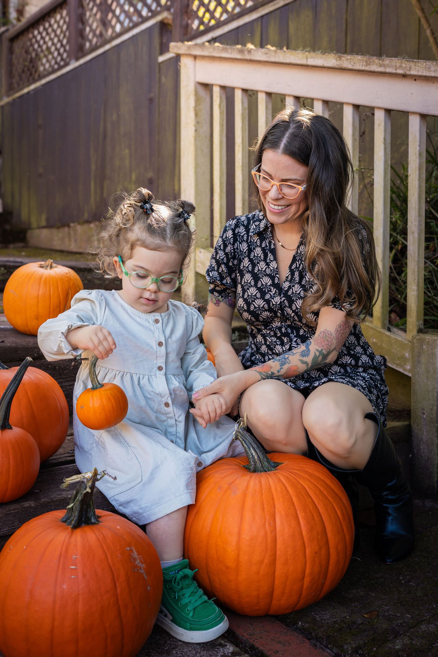 A mother and child share tender moments while sitting next to large orange pumpkins on a porch.