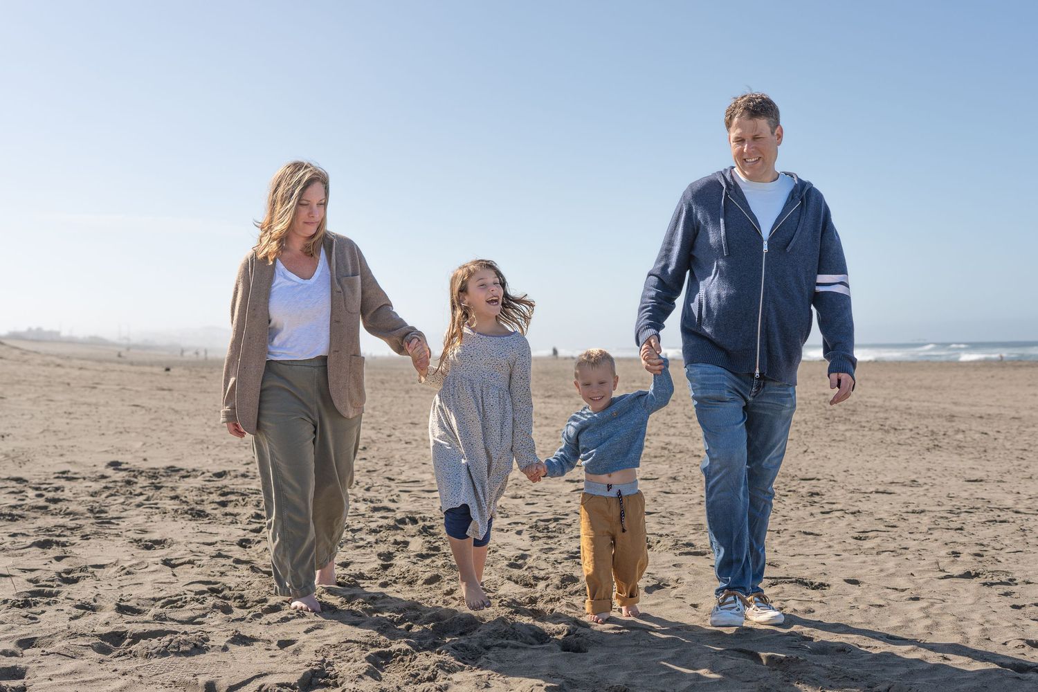 A family walks together along a scenic beach on a sunny day with waves and sand in the background.