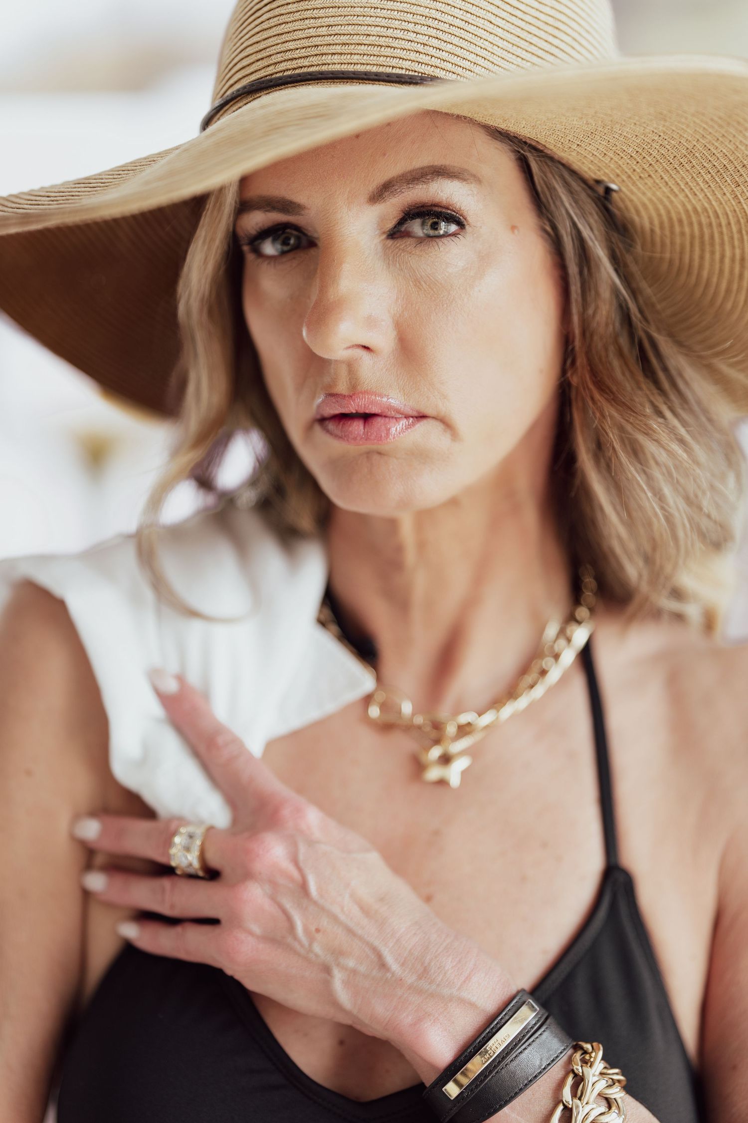 A portrait of someone wearing a wide-brimmed sun hat and gold jewelry.