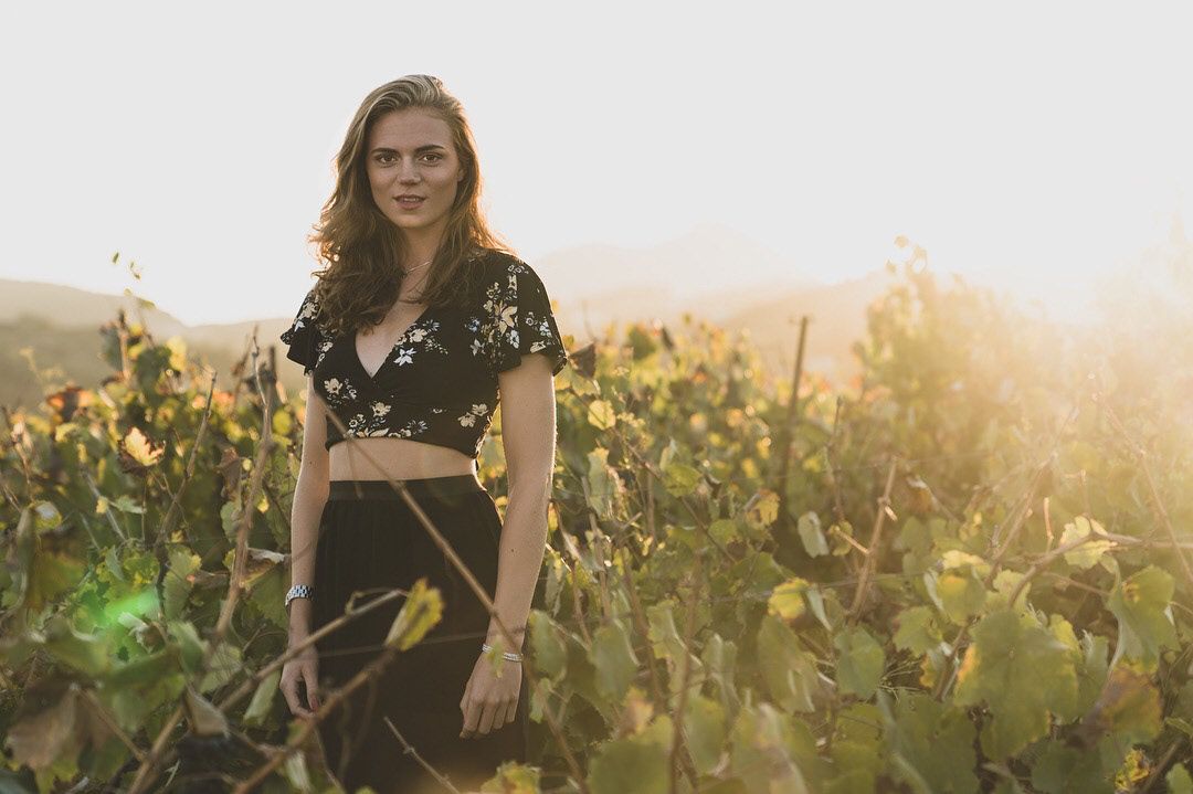 Portrait of a person in a floral crop top standing in a scenic vineyard at golden hour.