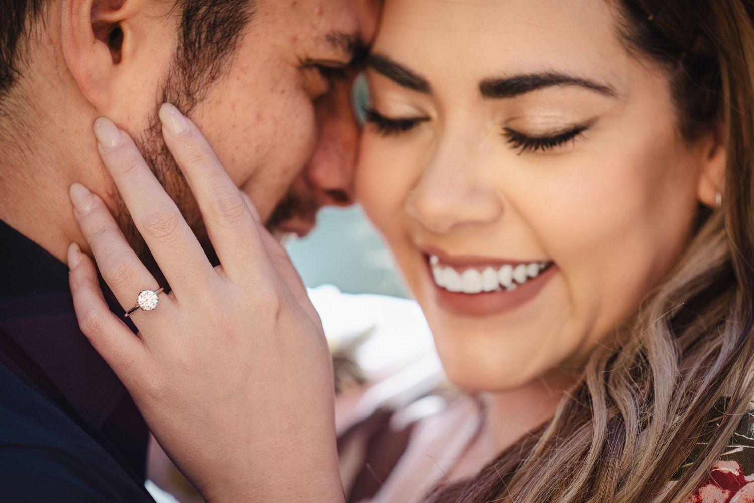 Close-up engagement photo showing a sparkly diamond ring and tender embrace.