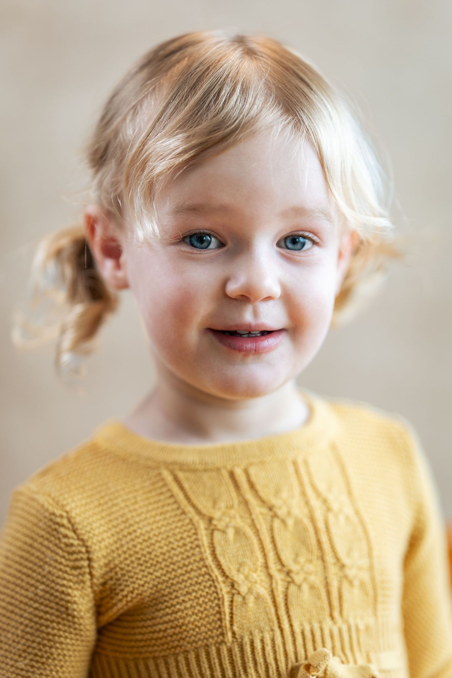 A young child wearing a yellow knit sweater smiles at the camera.