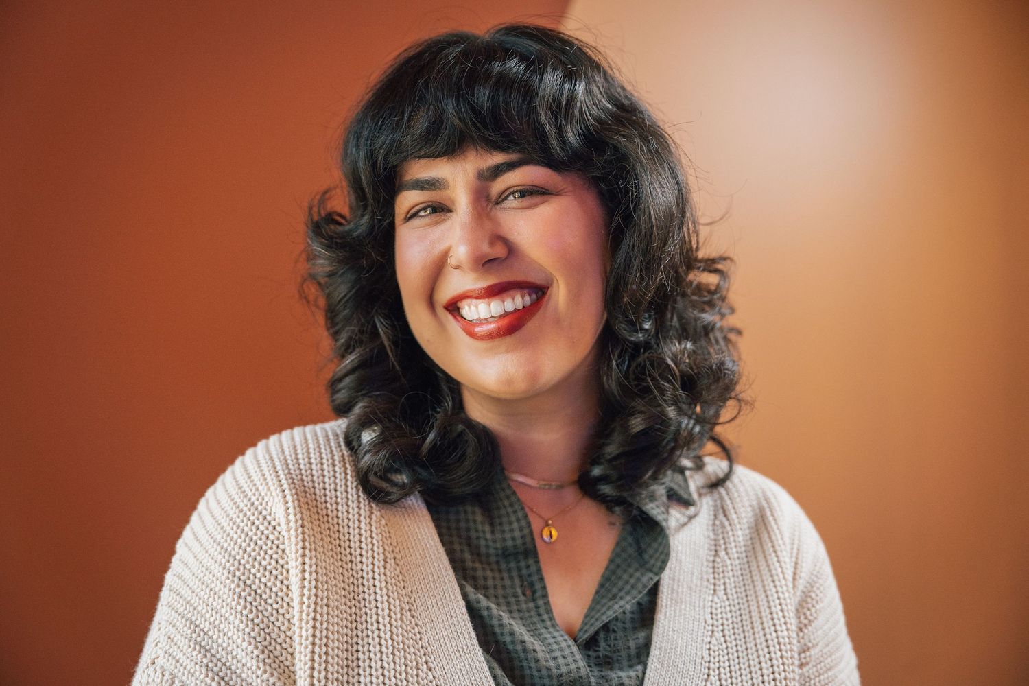 Portrait of a person with dark curly hair wearing a white cardigan and smiling warmly.