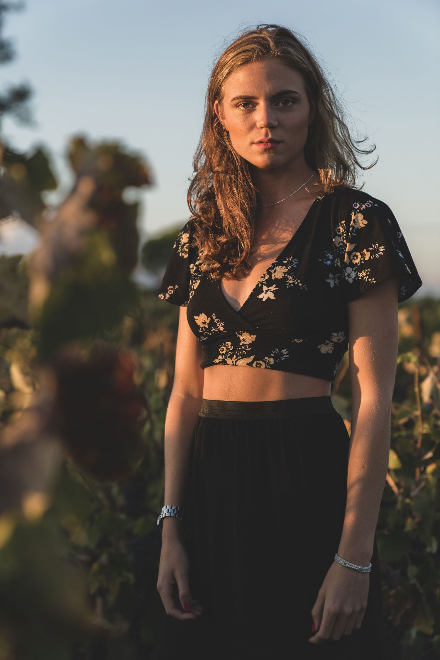 Portrait of someone wearing a floral crop top in a vineyard during sunset.