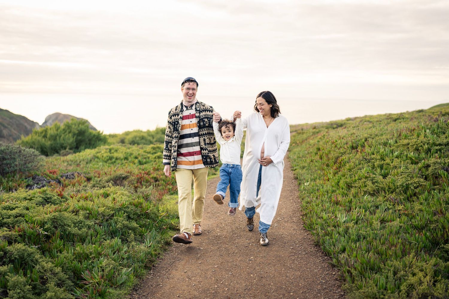 Family of three walking together on scenic hiking trail during sunset.