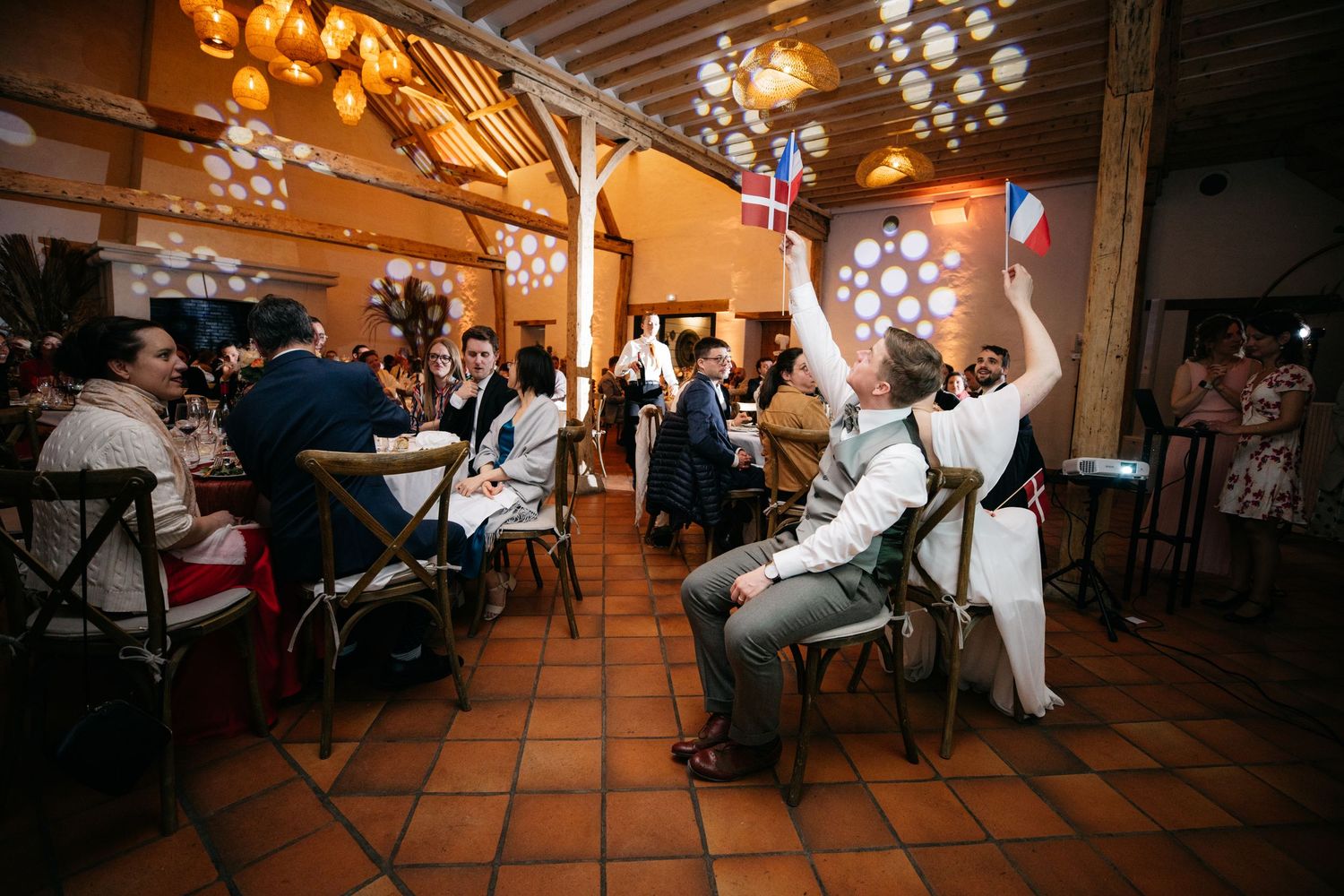Les invités agitent des éventails colorés lors d'une réception festive en intérieur, sous de chaleureuses guirlandes lumineuses.