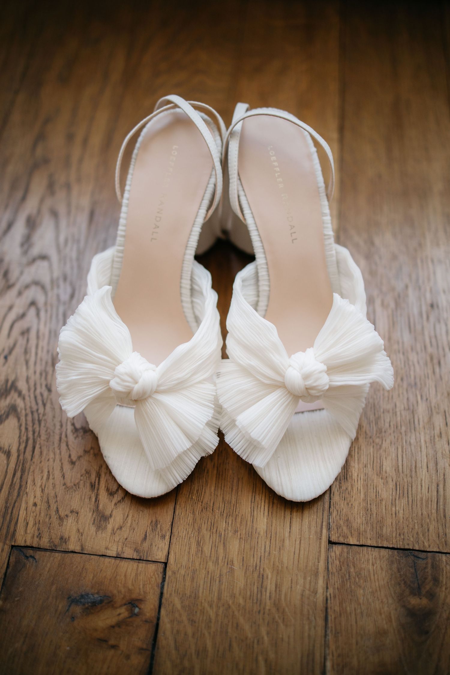 Chaussures de mariée blanches avec des détails d'arc délicats exposés sur un plancher en bois rustique.