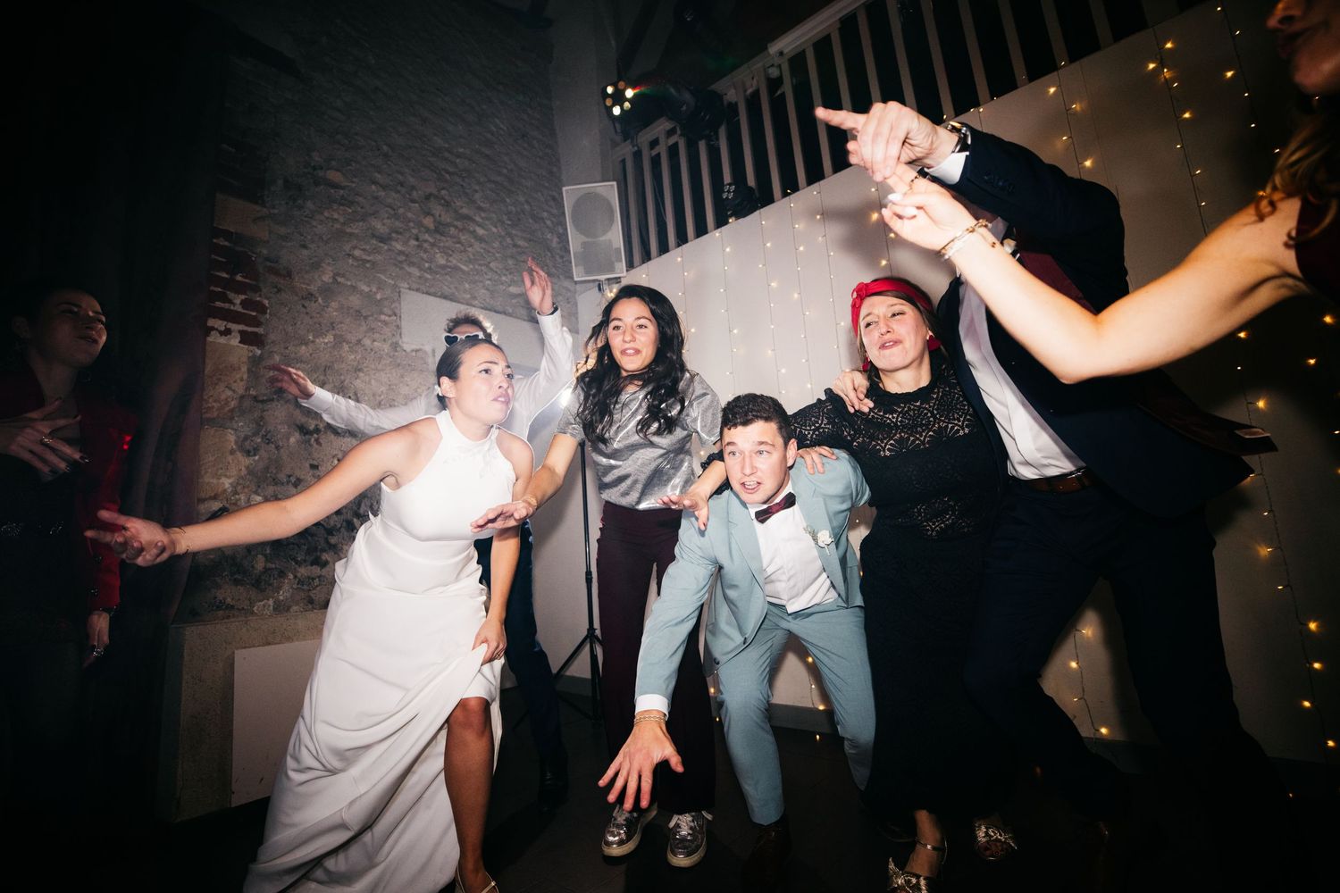 La mariée et ses amies dansant avec énergie lors d'une réception de mariage, illuminée par des guirlandes lumineuses.