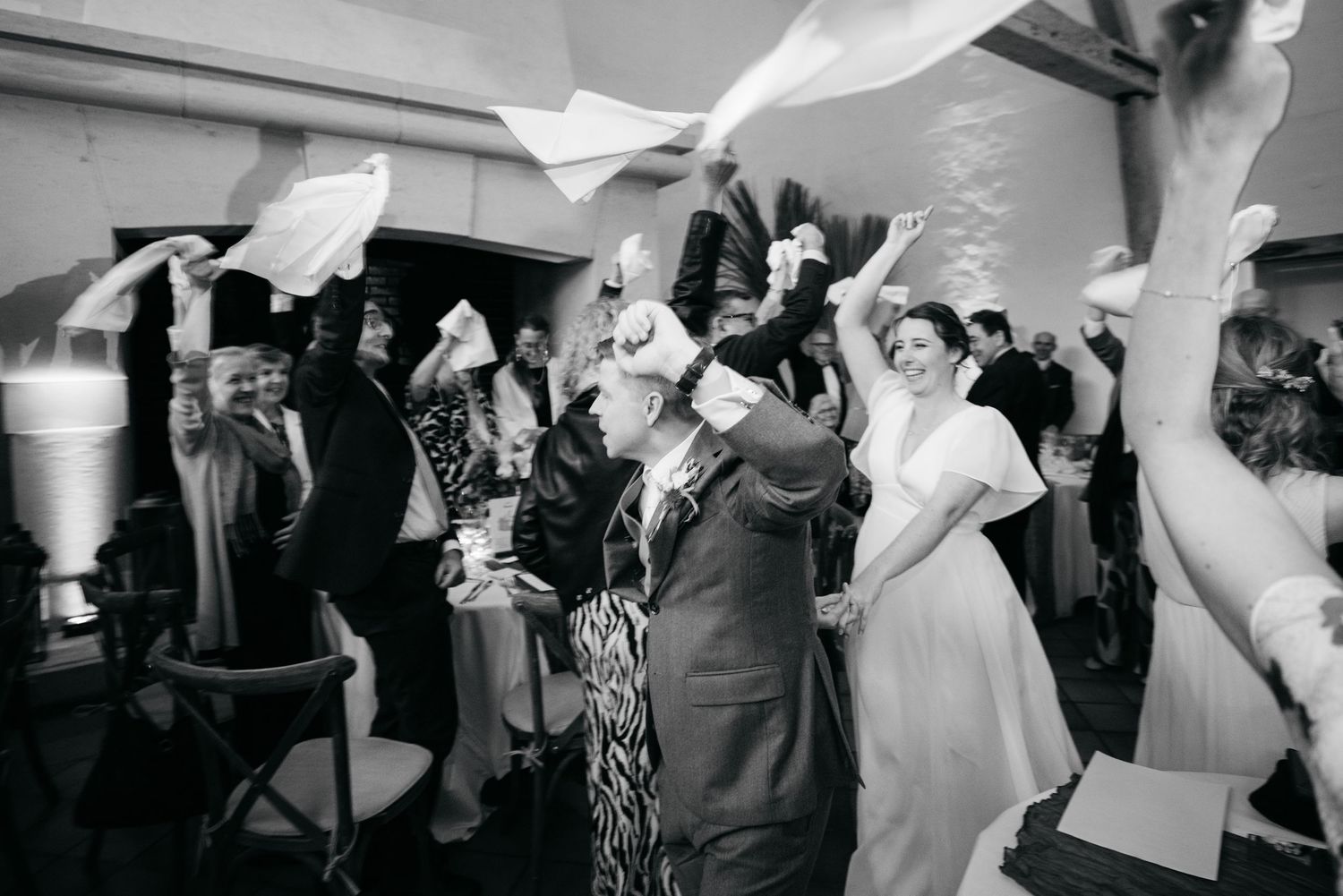 Photo en noir et blanc d'invités agitant des serviettes sur la piste de danse lors d'une joyeuse réception de mariage.
