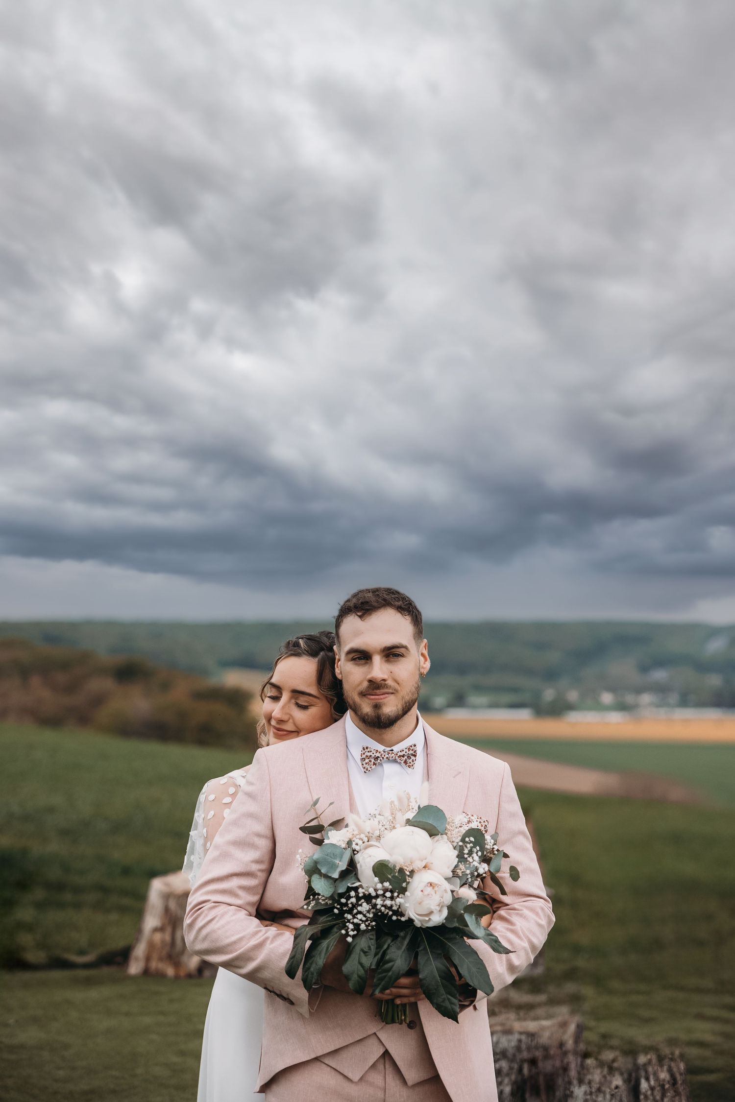 Un portrait de mariage spectaculaire contre des nuages d'orage de mauvaise humeur dans un paysage à flanc de colline.