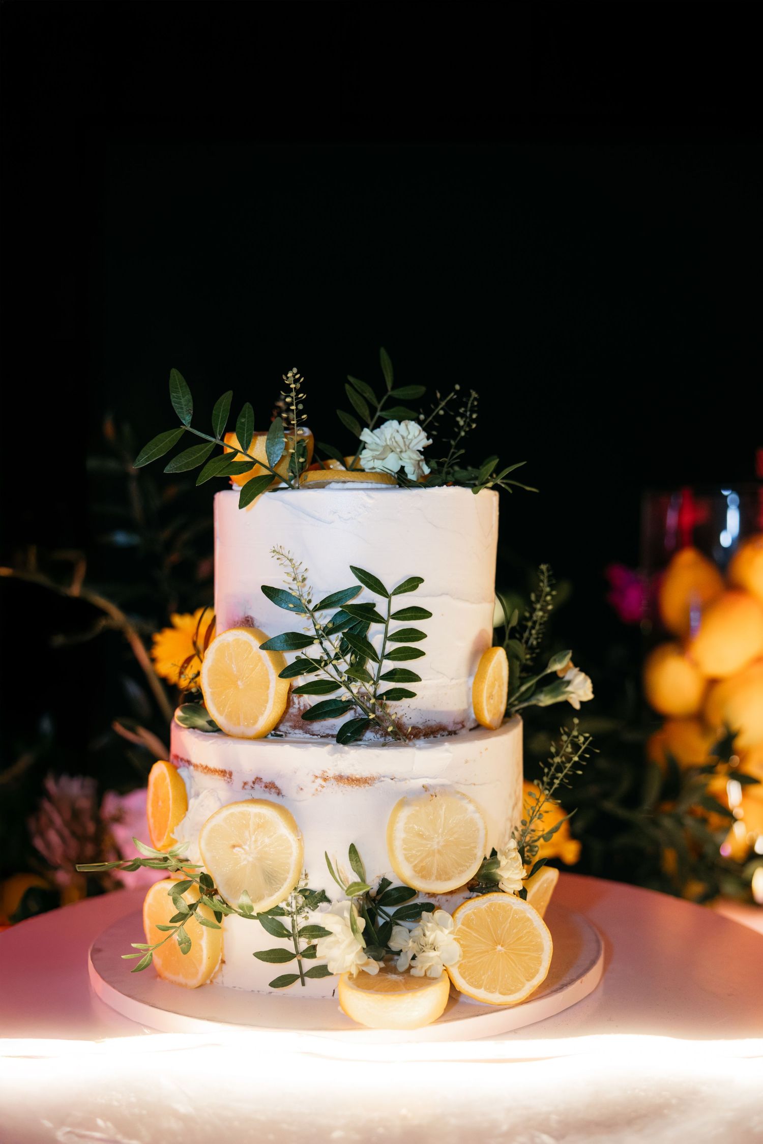 Gâteau de mariage blanc décoré de tranches de citron frais et de feuilles d'eucalyptus illuminées à l'écran.