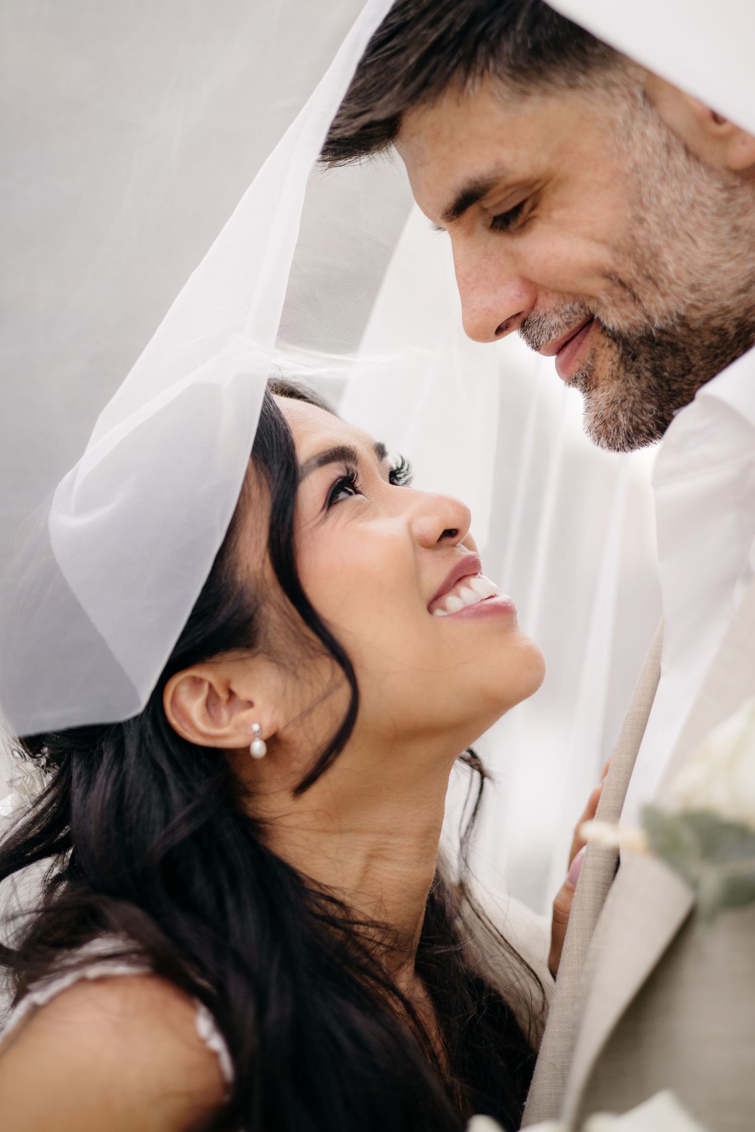 Les mariés partagent un moment intime sous un voile blanc, se souriant l'un à l'autre le jour de leur mariage.