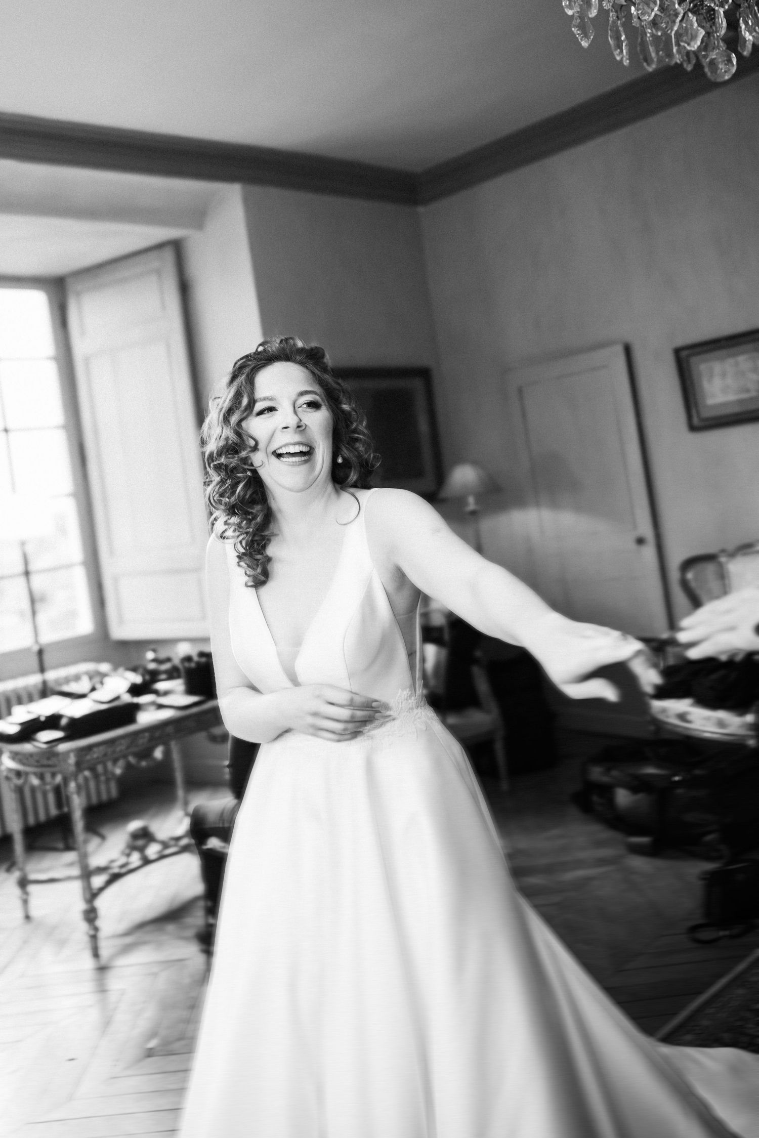 Une mariée joyeuse en robe blanche rit et tournoie dans une pièce élégante pendant les préparatifs du mariage, photographie en noir et blanc