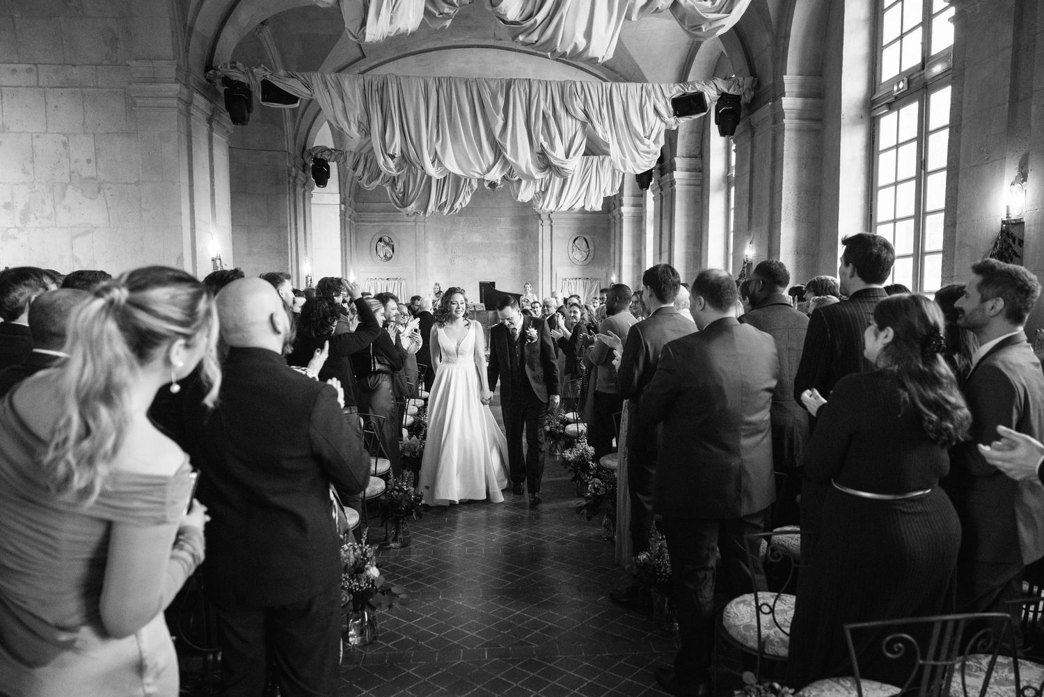 Photo de cérémonie de mariage en noir et blanc montrant la mariée et le marié à l'autel dans une élégante salle remplie d'invités.