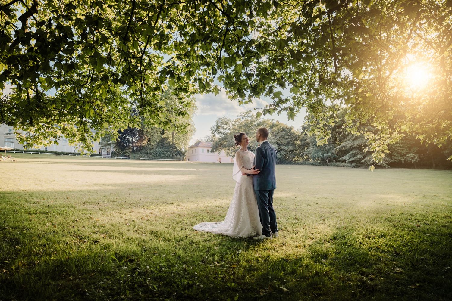 Un couple partage un moment intime dans une prairie ensoleillée pendant l'heure dorée alors que la lumière du soleil traverse les branches