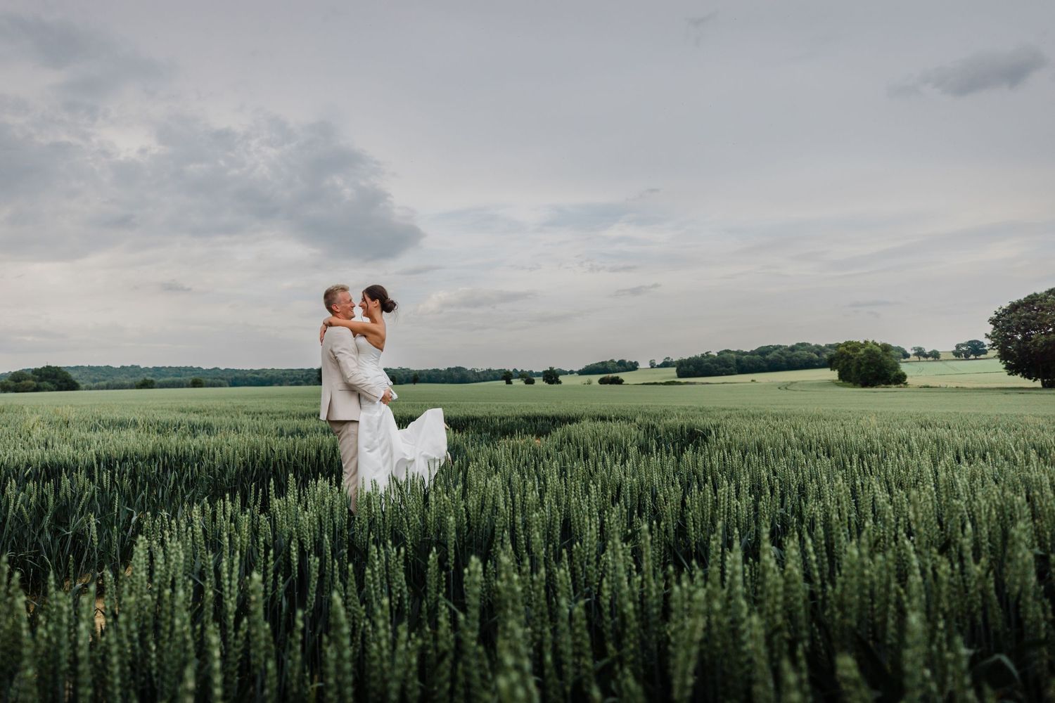 Un couple romantique s'embrasse dans un champ de blé verdoyant sous un ciel nuageux dramatique le jour de leur mariage.