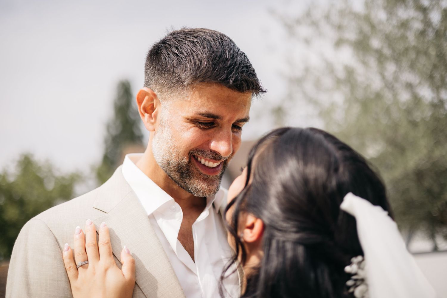 Le marié souriant, en costume beige, embrasse la mariée en extérieur lors de la cérémonie de mariage.