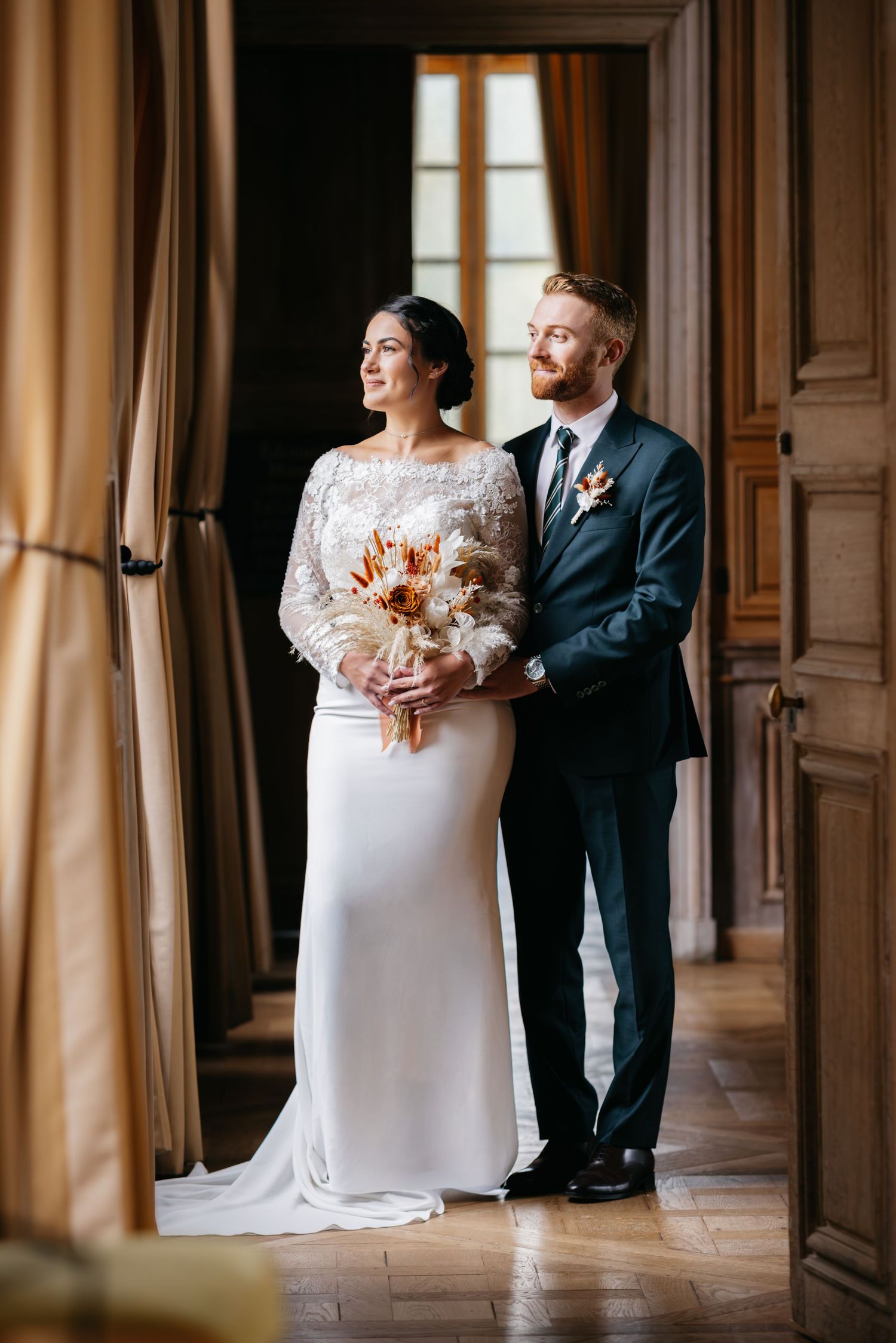 Une mariée et un marié posent ensemble dans un couloir élégant avec des lambris en bois ornés et des rideaux de couleur crème.
