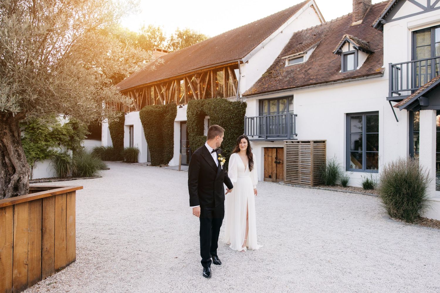 Un couple de mariés marche sur un chemin pavé à l'extérieur d'un lieu rustique pendant le coucher de soleil de l'heure d'or.