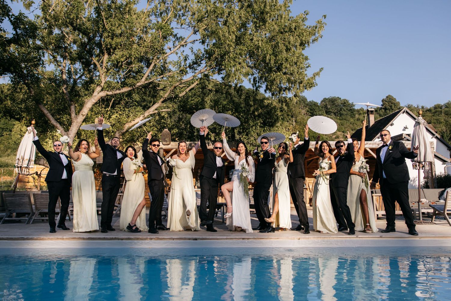 Les membres de la fête de mariage s'alignent le long du bord d'une piscine pour une photo de groupe lors d'une réception en plein air.