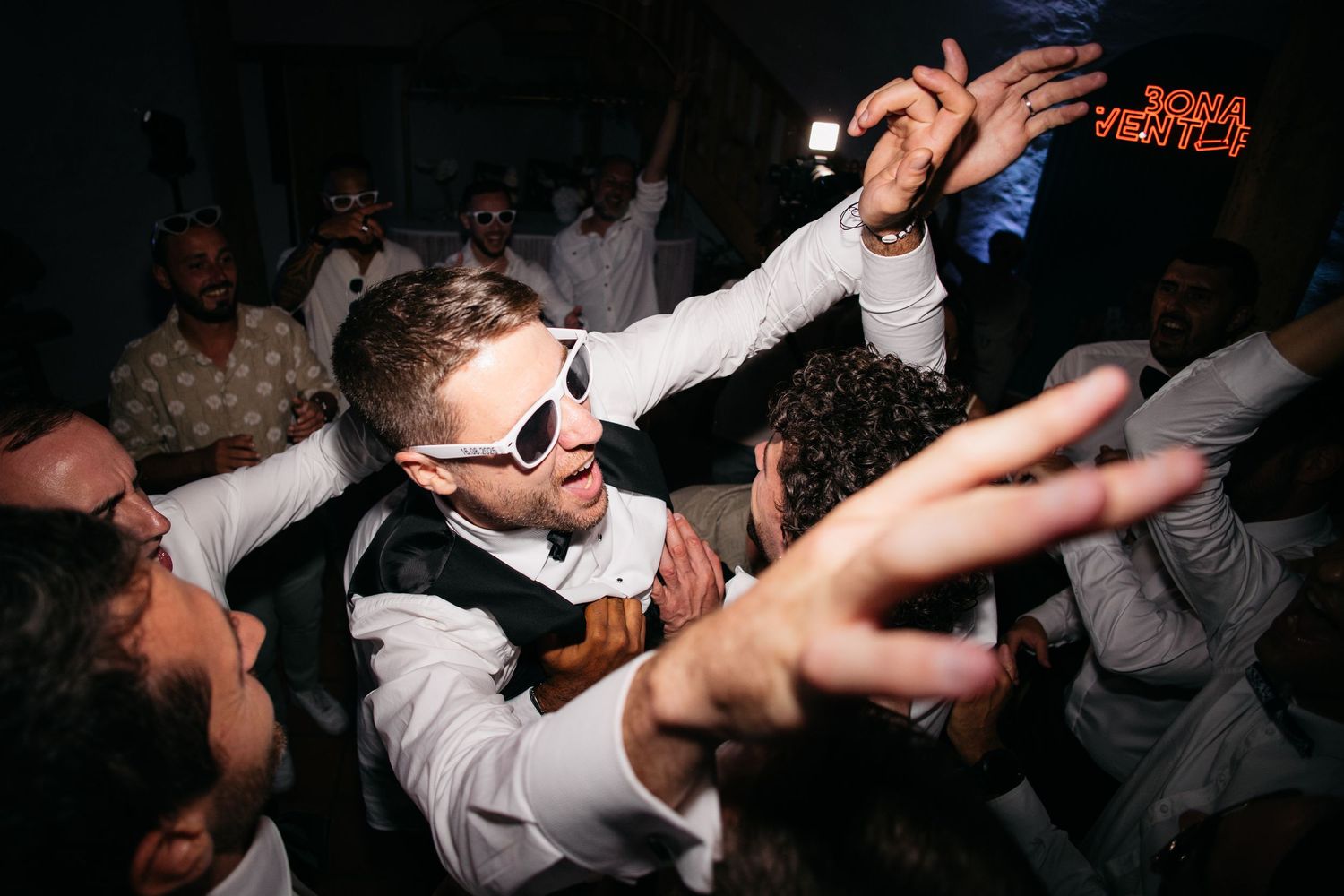 Les invités de mariage dansent énergiquement sur une piste de danse sombre lors d'une célébration de réception.