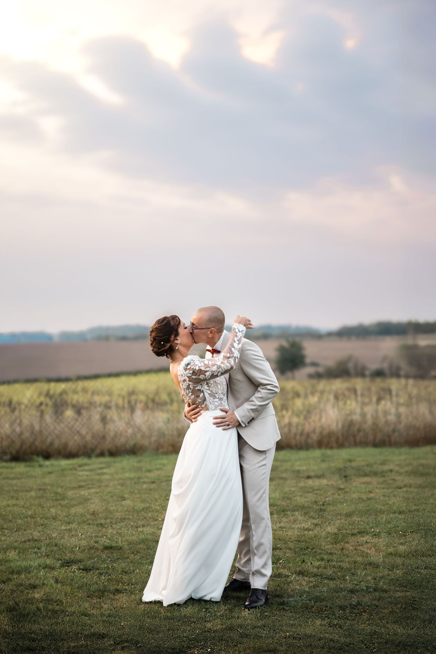 Un couple en tenue de mariage s'embrasse et danse dans une prairie pittoresque au coucher du soleil avec des collines en arrière-plan.
