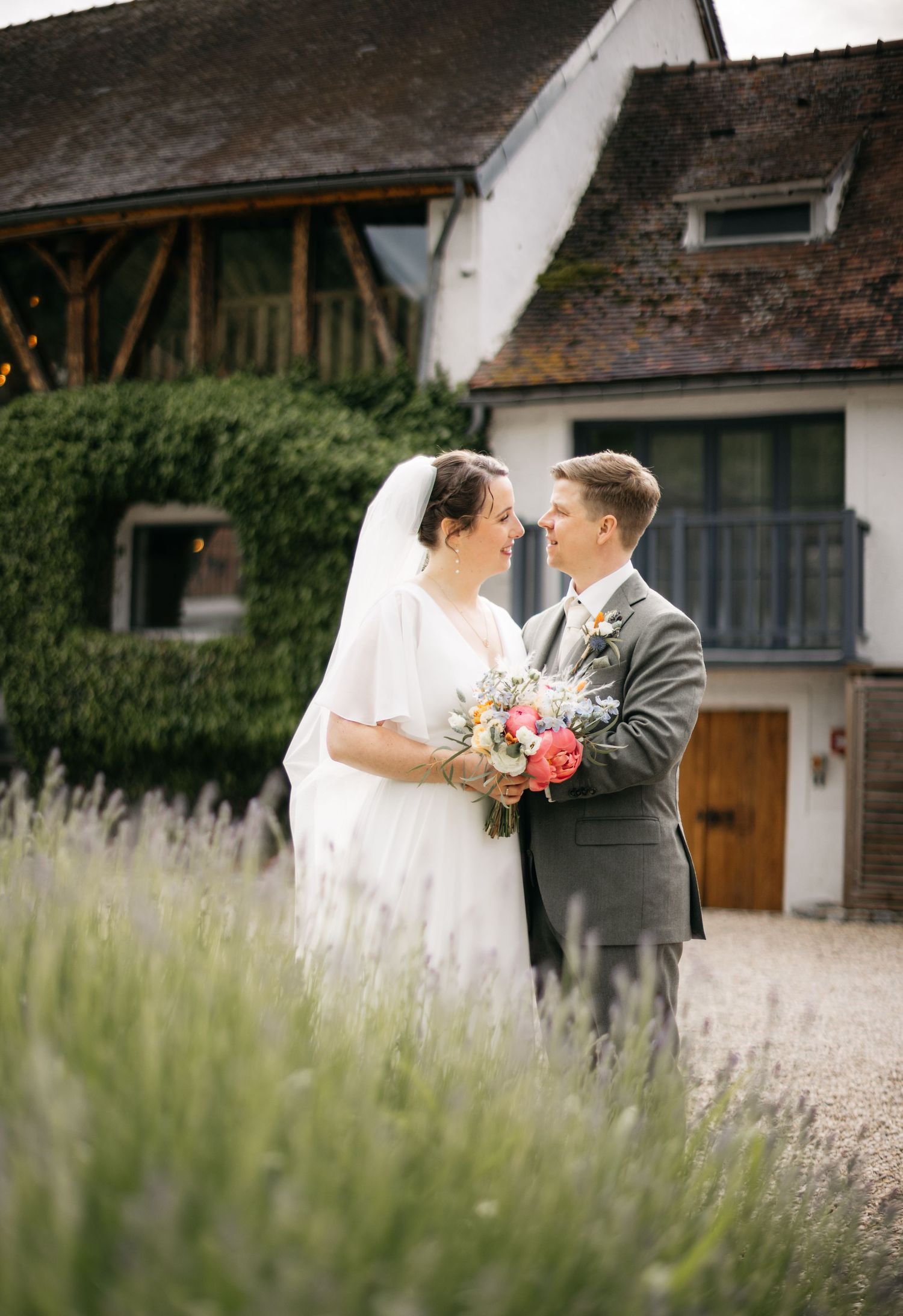 Les mariés partagent un moment romantique dans un champ de lavande à l'extérieur d'une grange blanche rustique.