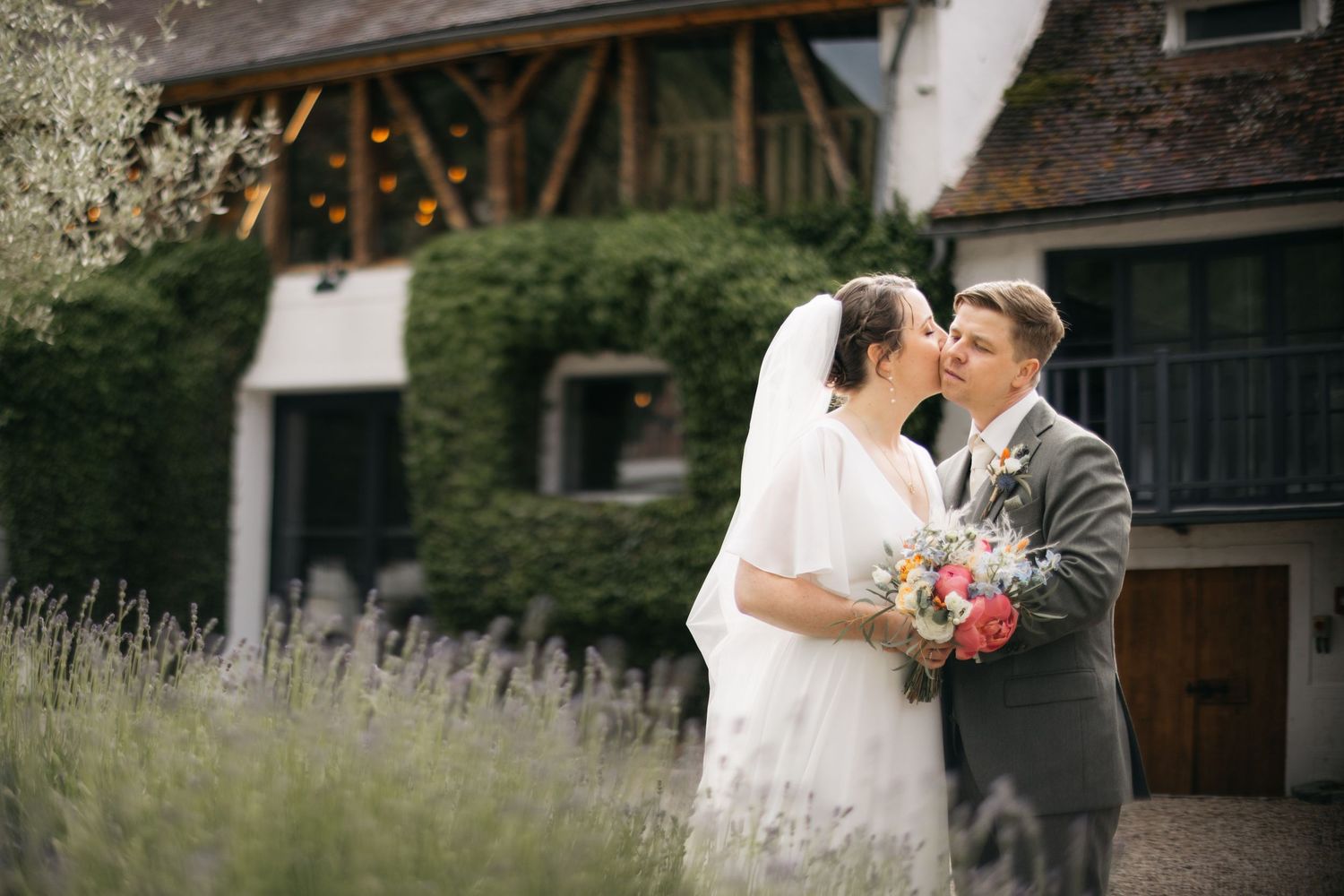 Bride and groom share a romantic moment in front of an ivy-covered venue surrounded by lavender.