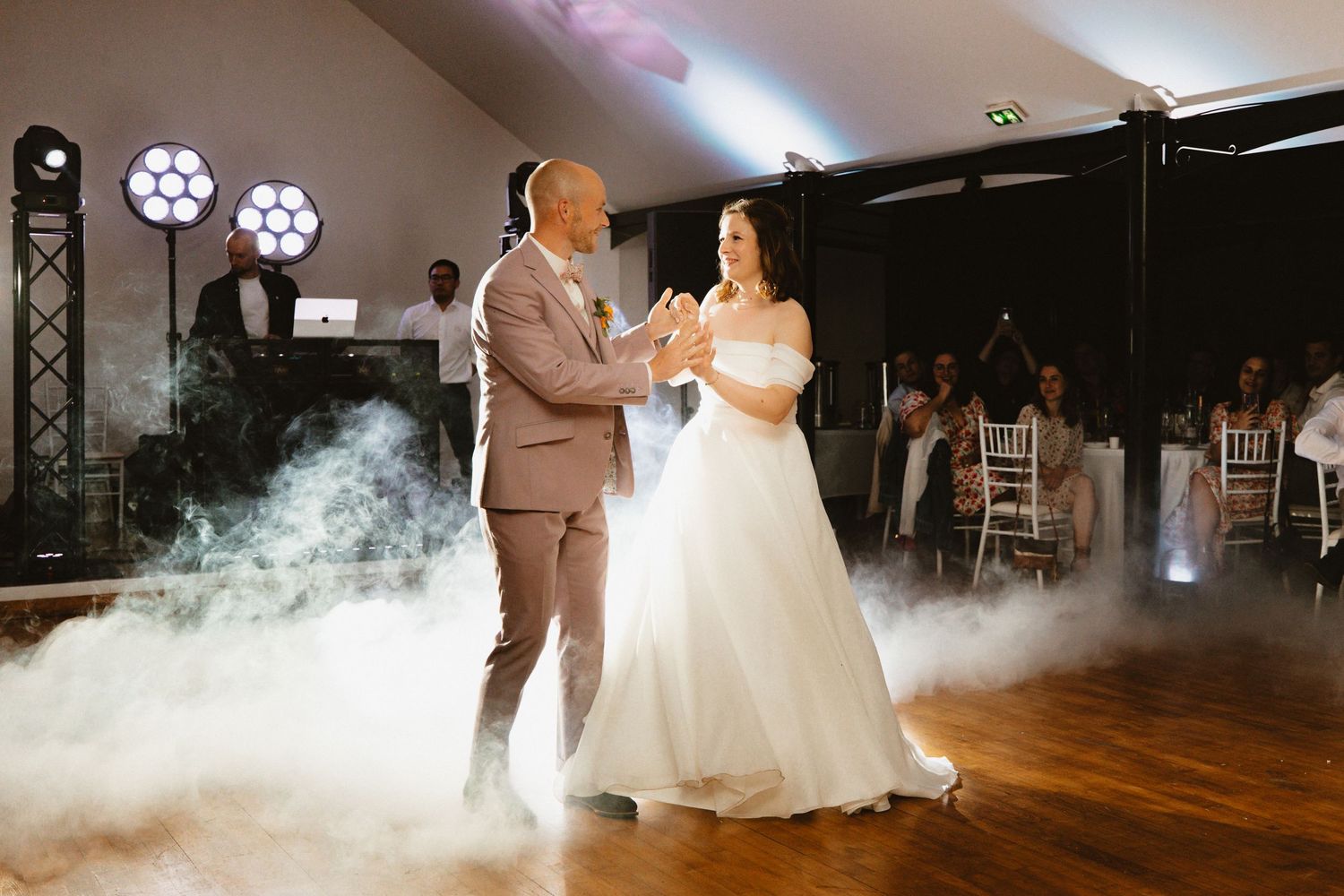 Les mariés partagent leur première danse sur une piste brumeuse lors d'une élégante réception de mariage.