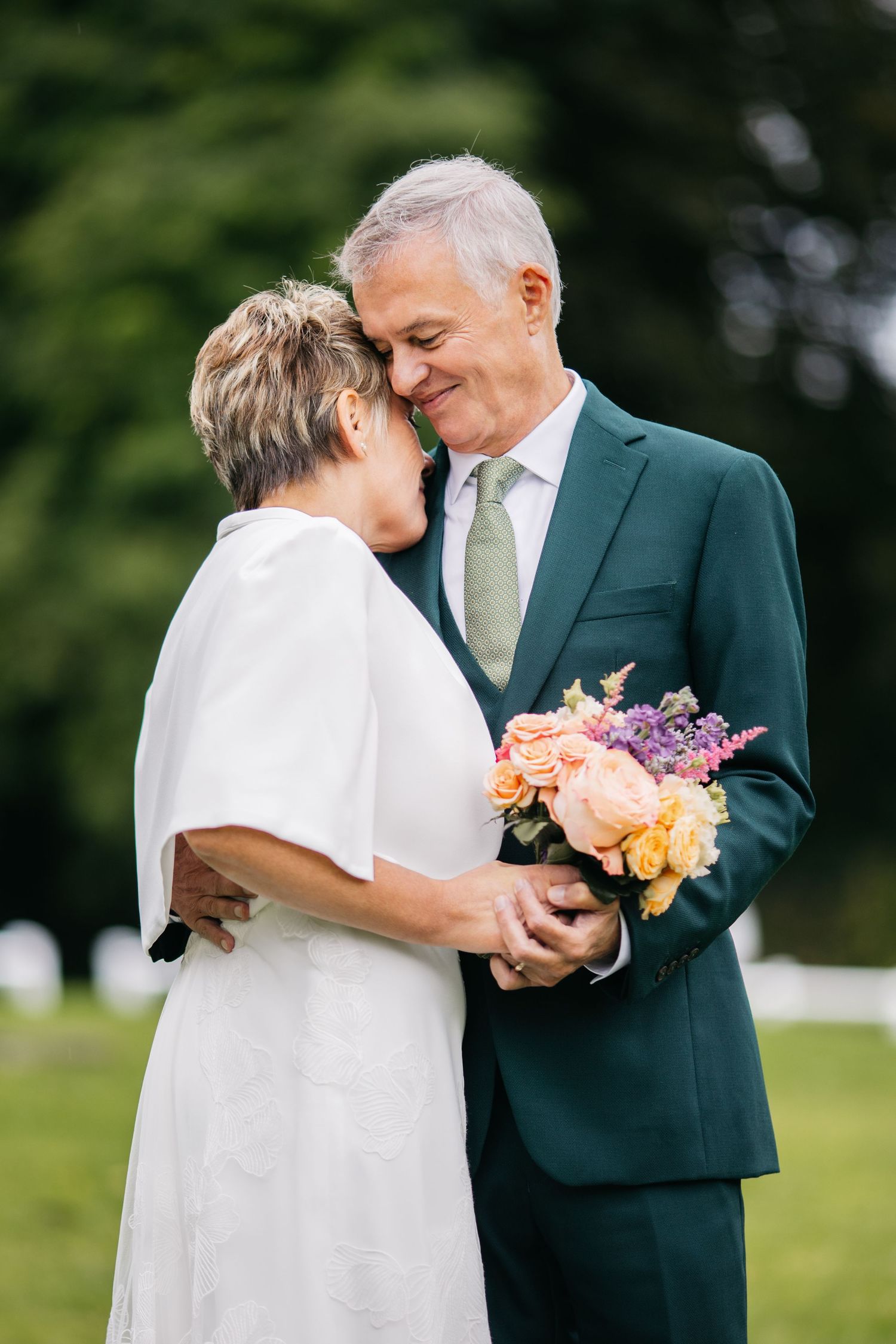 Couple en tenue de mariage partageant des moments intimes dans un jardin tout en tenant un bouquet coloré de fleurs.