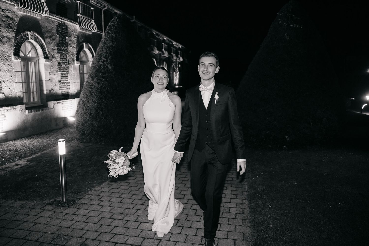 Des photos de mariage en noir et blanc montrent un couple marchant ensemble sur un chemin de briques la nuit.
