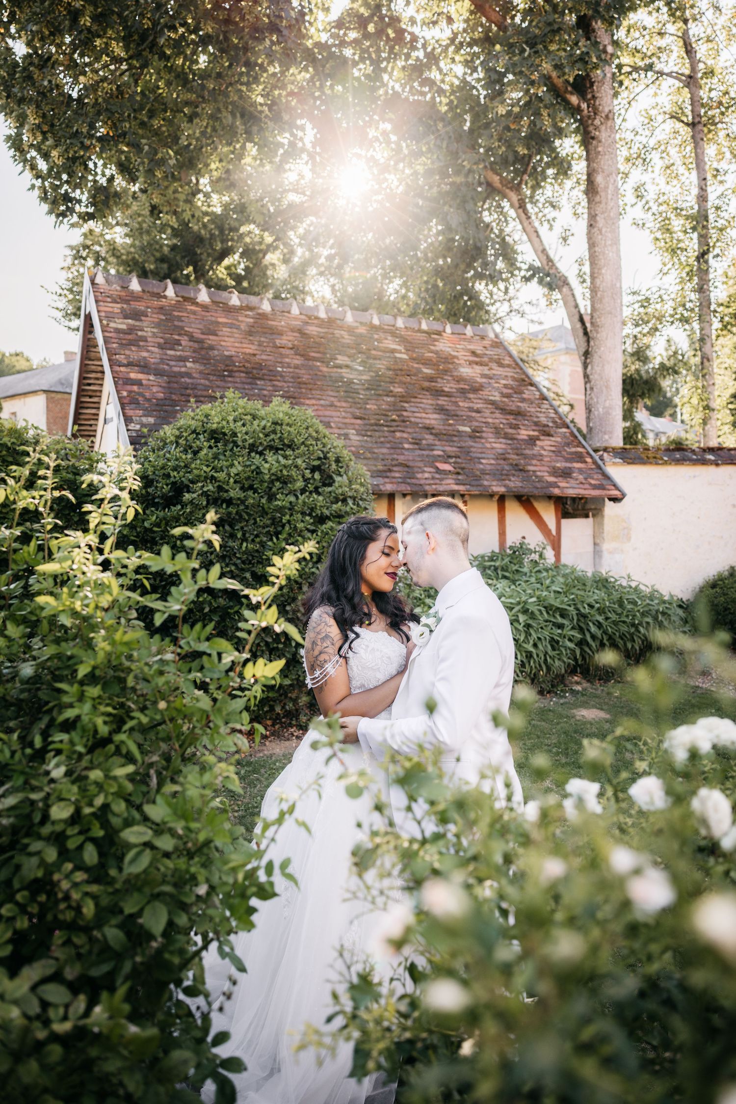 Les mariés partagent un moment romantique dans un jardin luxuriant, baigné de soleil doré, près d'un charmant cottage.
