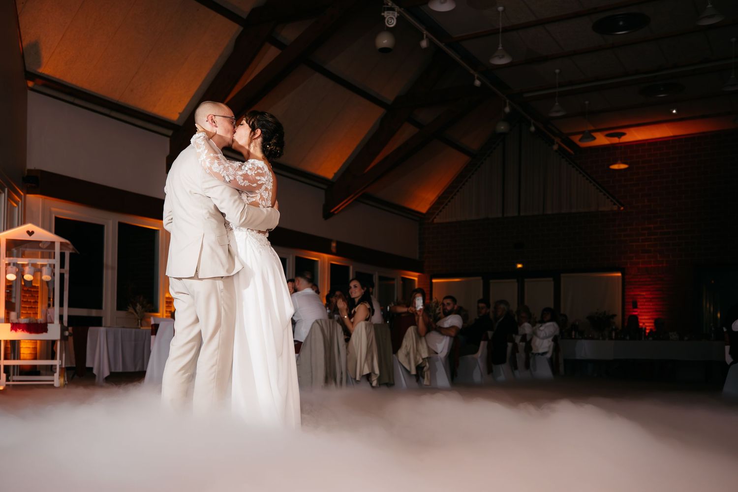 Les mariés partagent leur première danse entourés d'une brume romantique sur la piste de danse d'une réception de mariage.