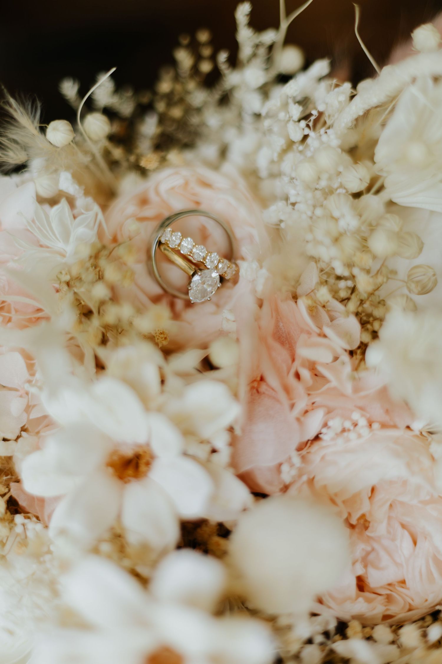 Gold diamond engagement ring and wedding band nestled among blush pink peonies and white baby's breath bouquet.