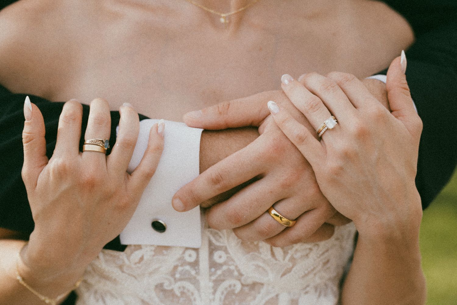Close-up of bride and groom hands with gold wedding rings resting on white lace wedding dress.
